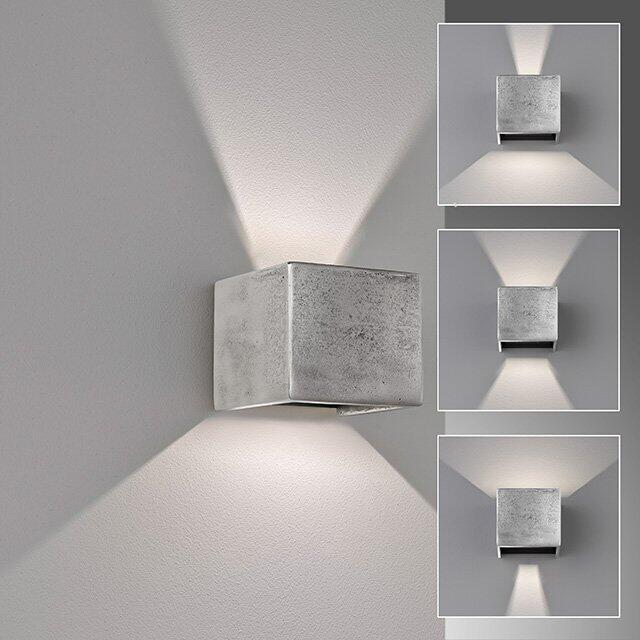 Wandleuchte Cog mit nickelfarbenem Finish an einer hellgrauen Wand, zeigt das kubische Design und die indirekte, aufsteigende Lichtwirkung.