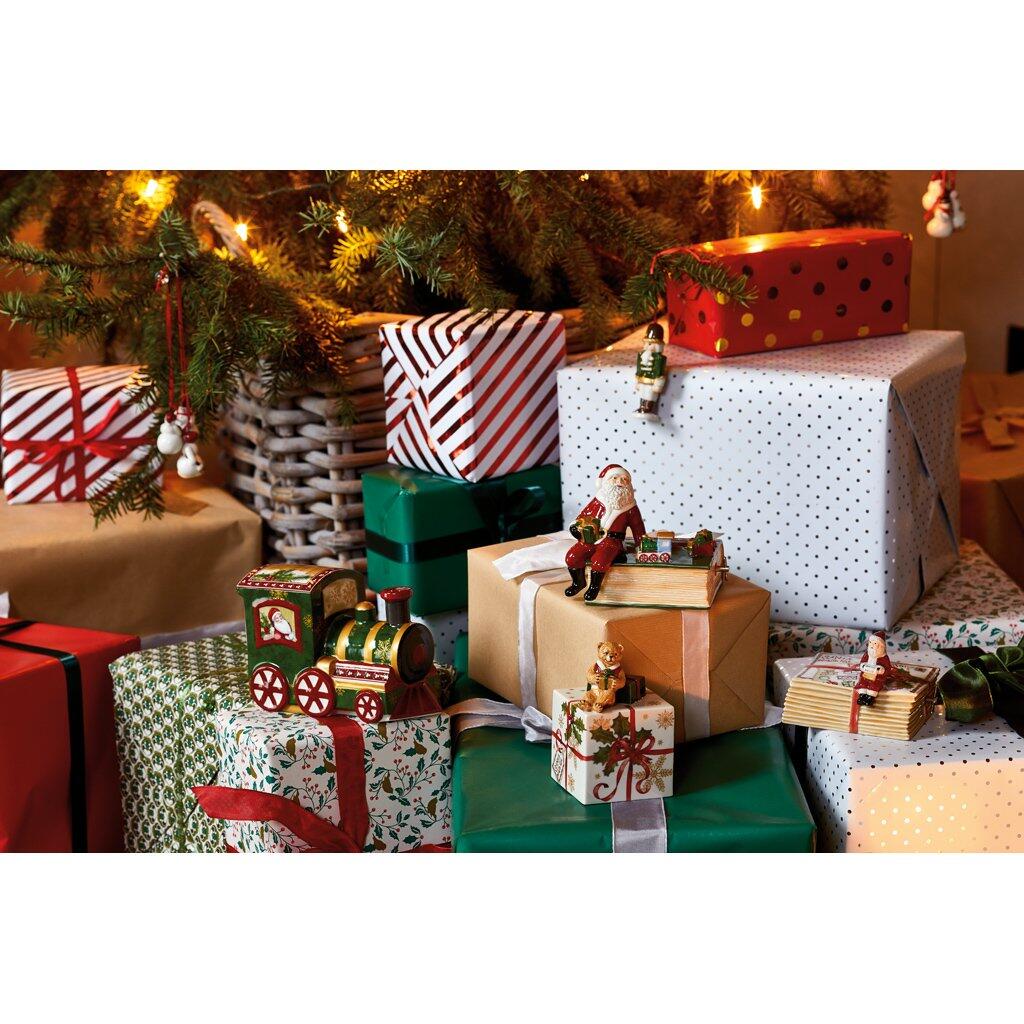 Festlich dekorierte Szene mit Geschenkboxen, einer Holz-Lokomotive mit Figuren und weihnachtlichen Ornamenten vor einem beleuchteten Tannenbaum.