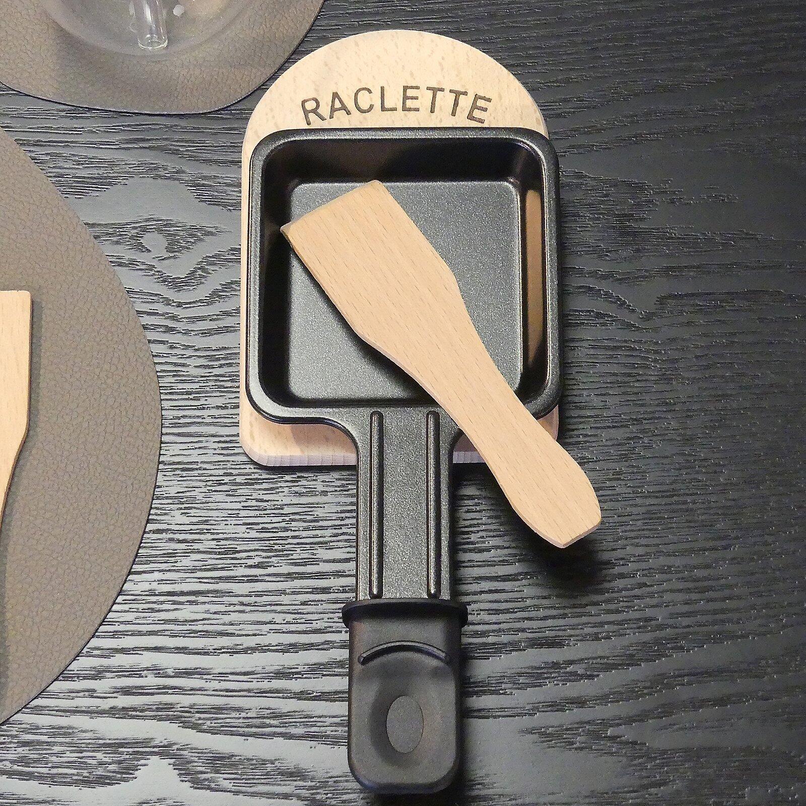 Raclette-Brettchen "Baar": Antihaftbeschichtetes, schwarzes Metallpfännchen mit abnehmbarem, grifflochartigem Holzgriff aus Vogelperspektive.