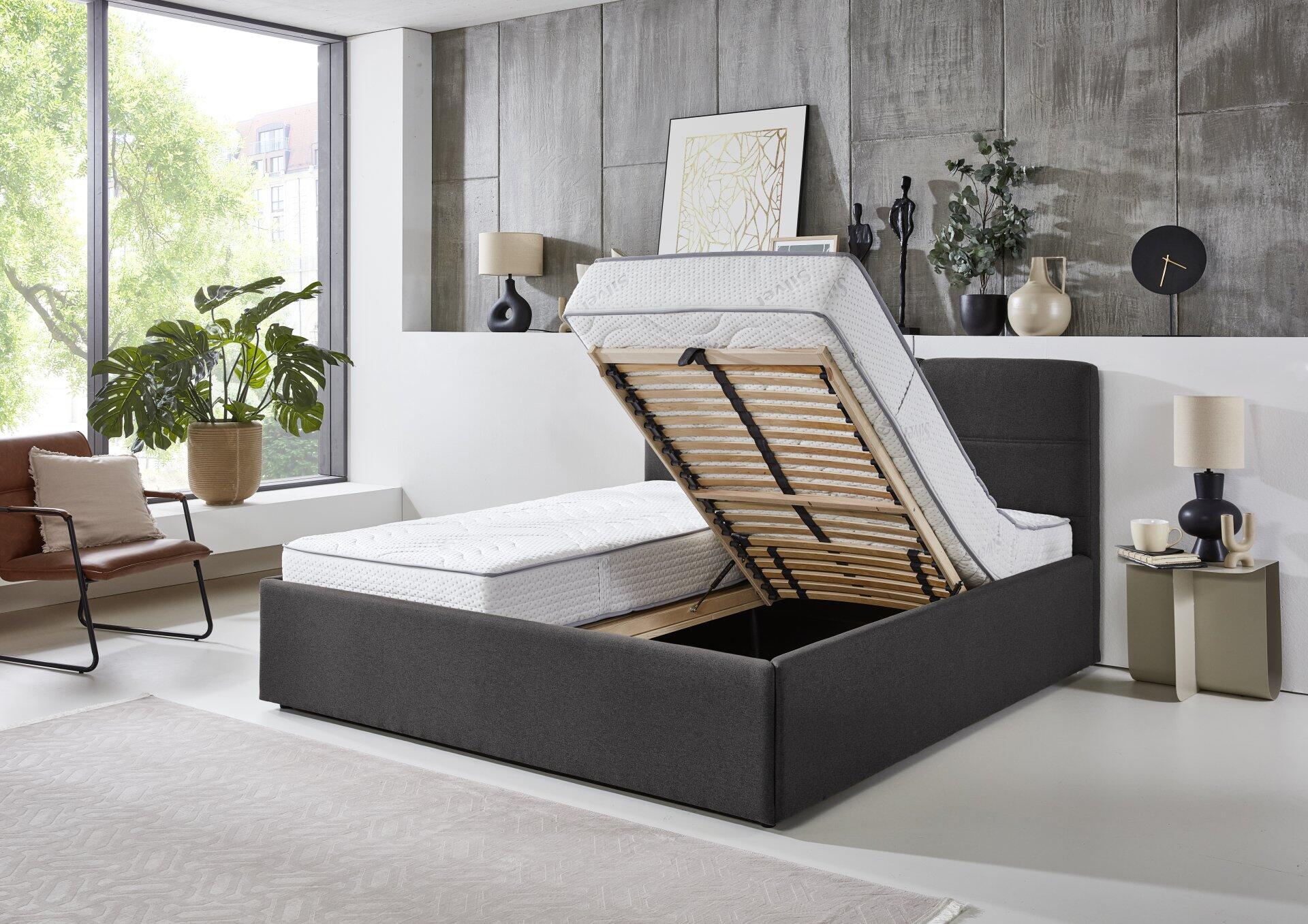 Polsterbett Durango PB100 mit grauem Stoffbezug und hochklappbarem Lattenrost, der Stauraum freigibt.