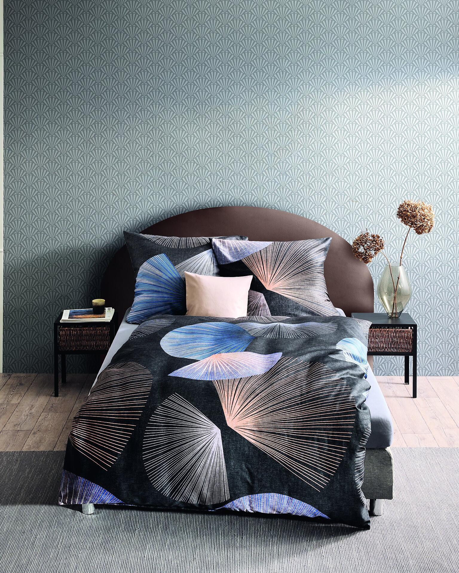 Schlafzimmer mit Bettwäsche Koya in Schwarz, mit einem abstrakten, blauen, rosa und schwarzen Fächer-Druck auf dem dunkelblauen Bettbezug und hellrosa Kissen.