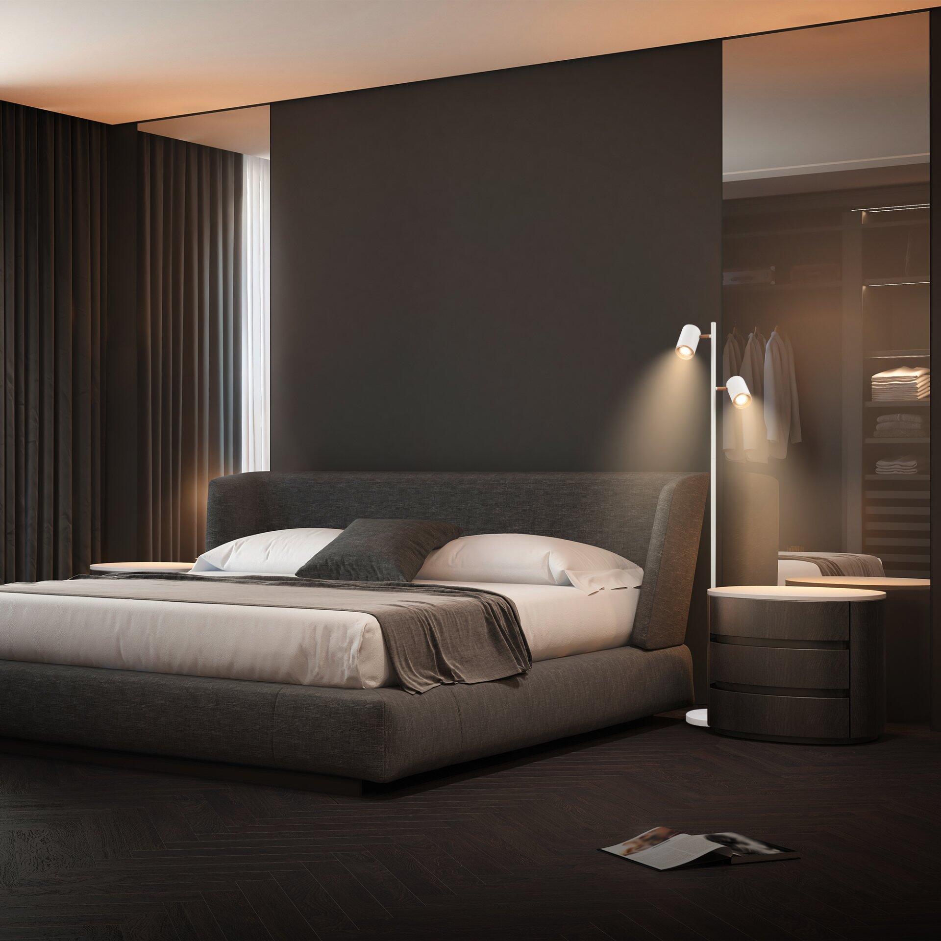 Stehleuchte Era mit schlankem Lampenfuß und zwei Armen neben einem modernen Bett in einem stilvoll eingerichteten Schlafzimmer.