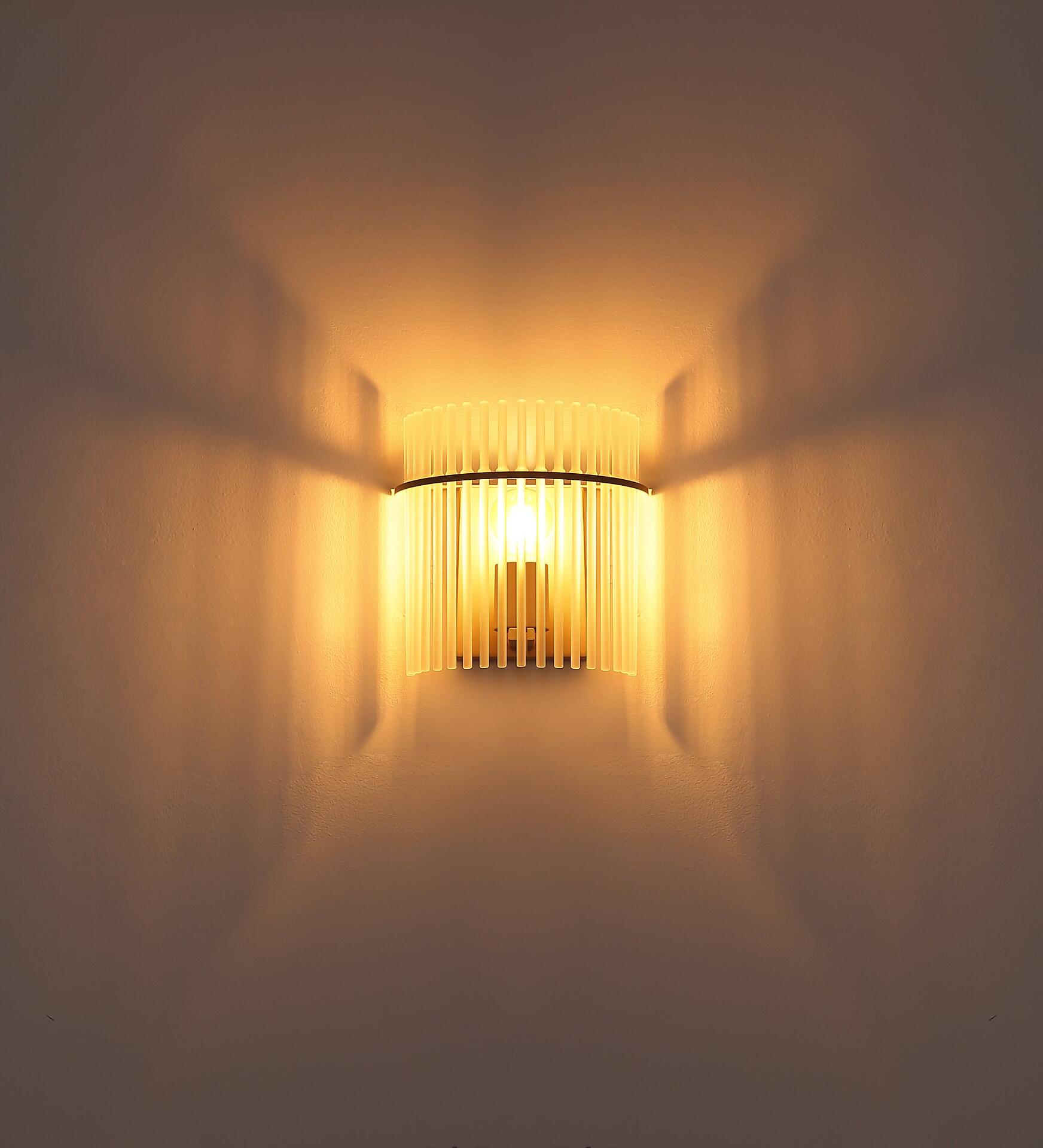 Wandleuchte GORLEY mit vertikalen Lamellen, die warmes Licht streuen und ein dekoratives Muster an der Wand erzeugen.