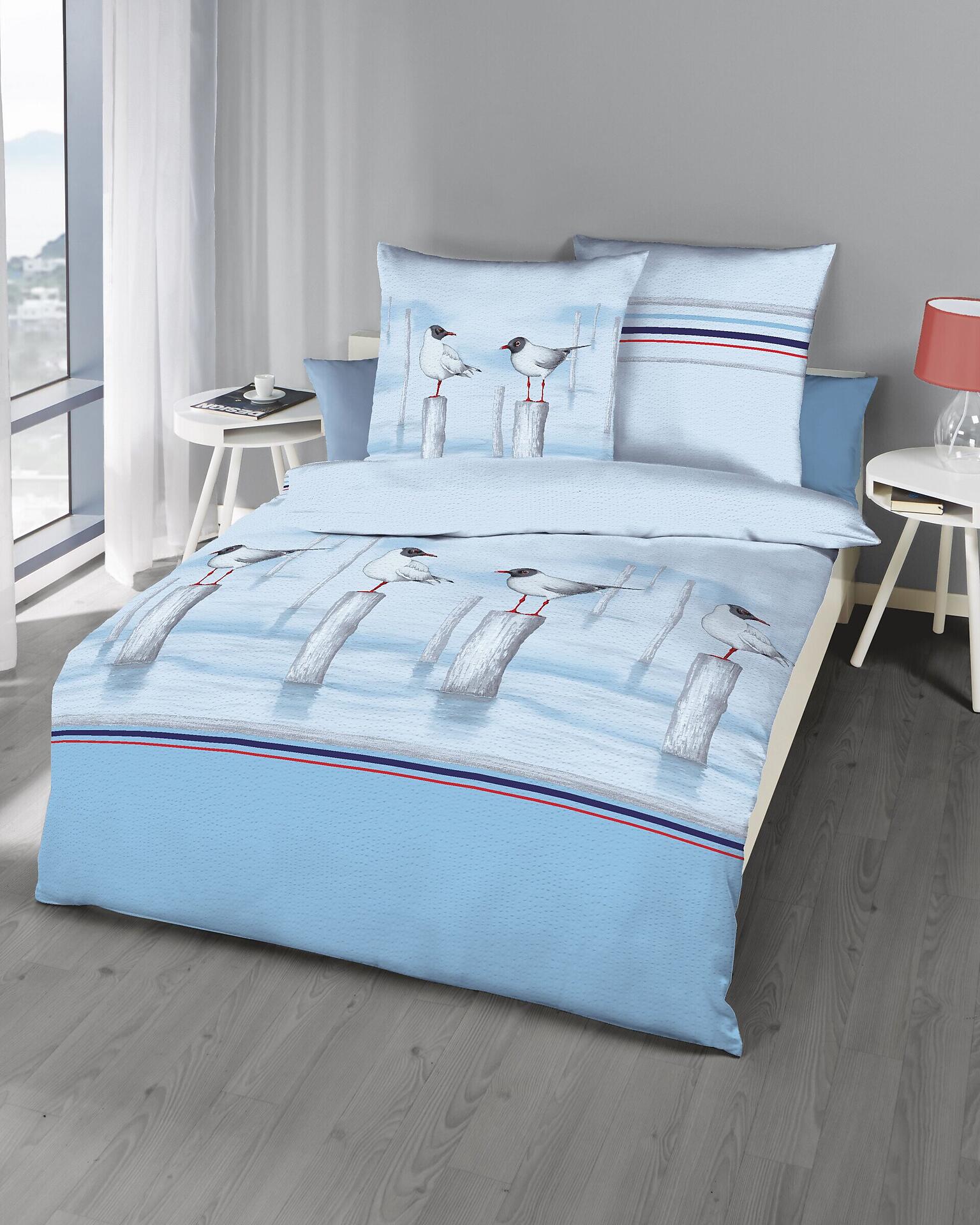 Bettwäsche Möwen: Hellblaue Bettwäsche aus 100 % Baumwolle mit Möwenmotiv und passenden Kissen auf einem Bett, aufgenommen aus einer frontalen Perspektive.