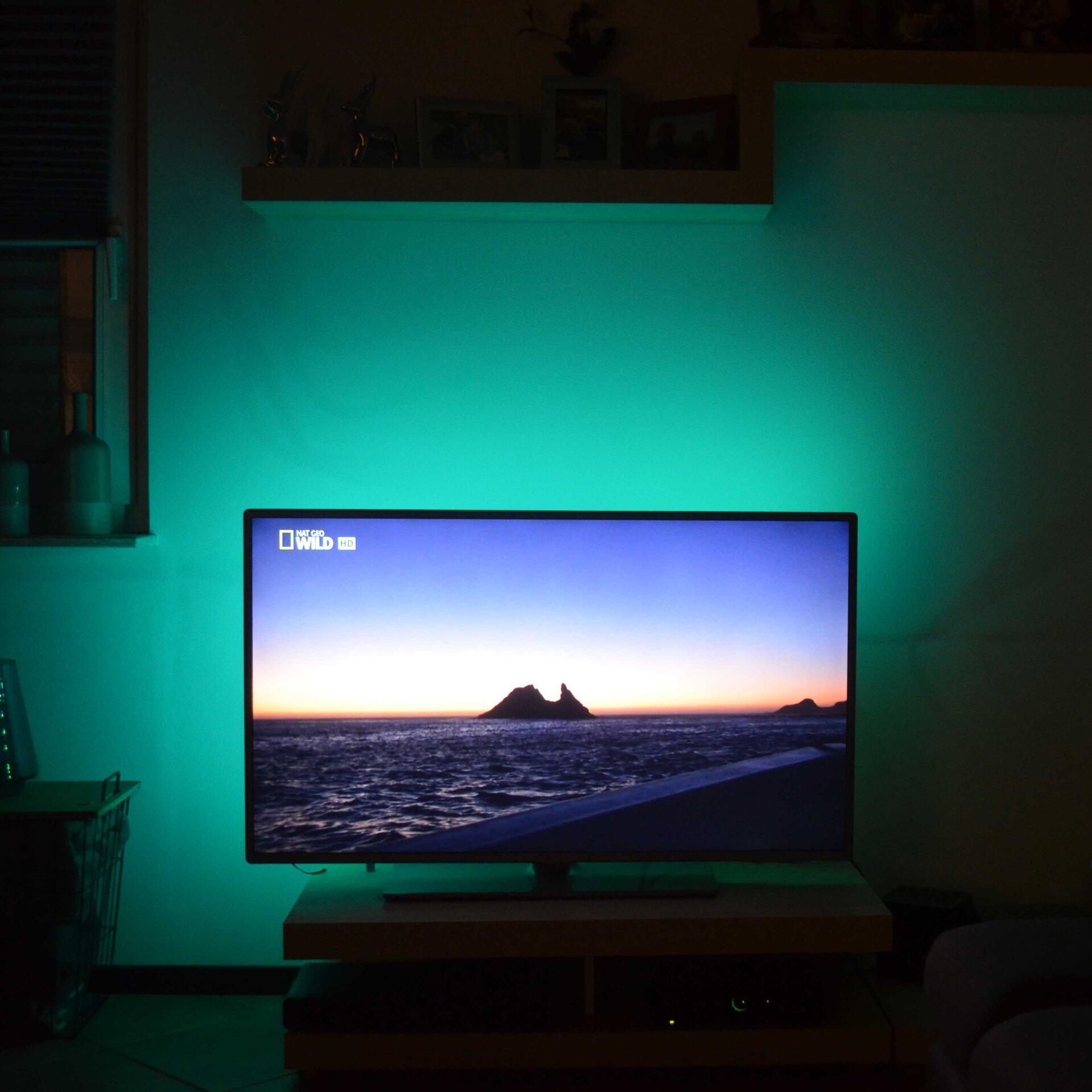 LED Band BRILO hinter dem Fernseher sorgt für eine stimmungsvolle, grüne Hintergrundbeleuchtung, die den Bildschirm betont und durch die leicht erhöhte Perspektive größer wirken lässt.