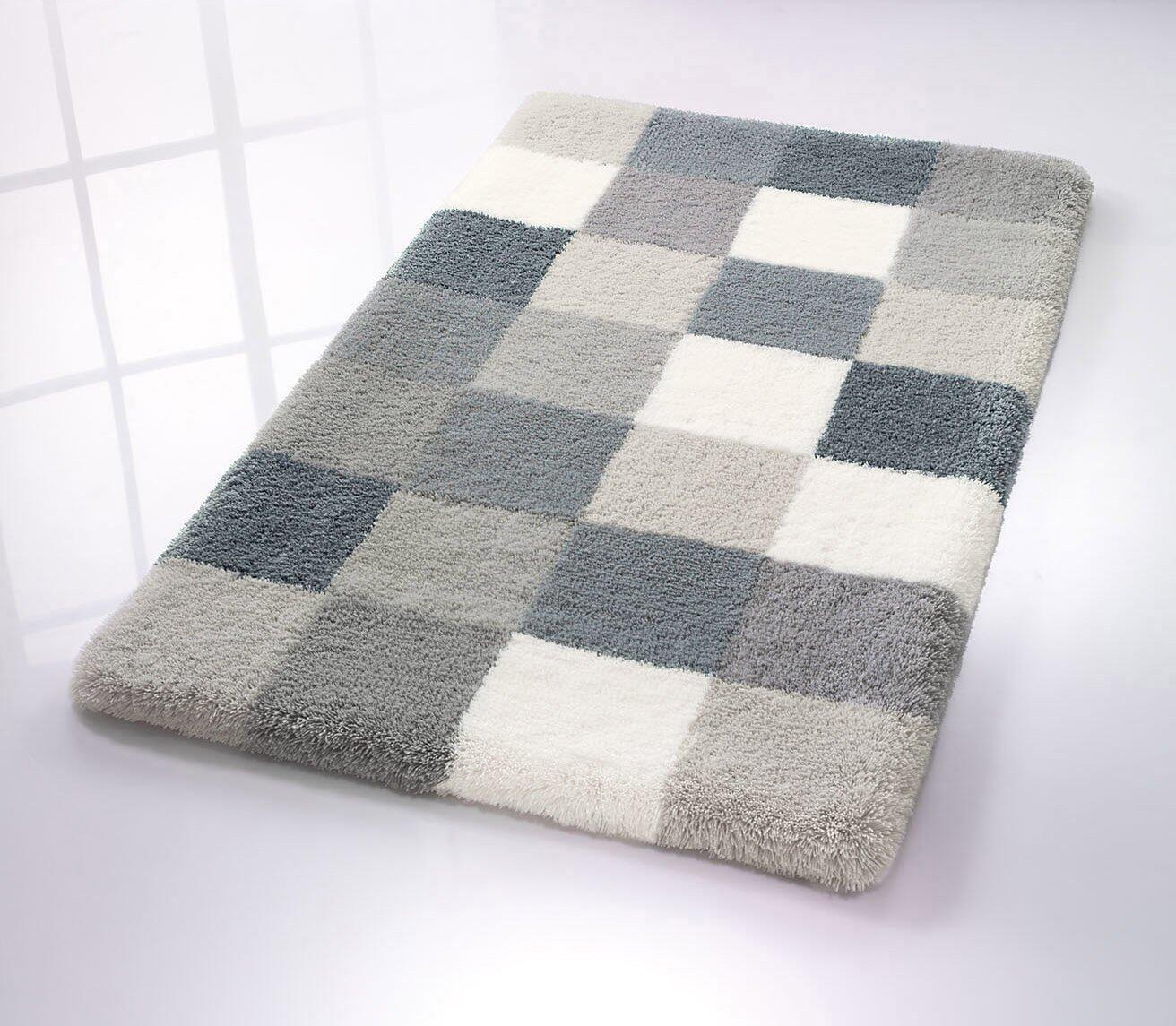 Quadratischer WC-Vorleger Caro aus weichem Flanell mit abgerundeten Kanten und Schachbrettmuster aus hellgrauen und dunkelgrau-blauen Quadraten, fotografiert von oben links.