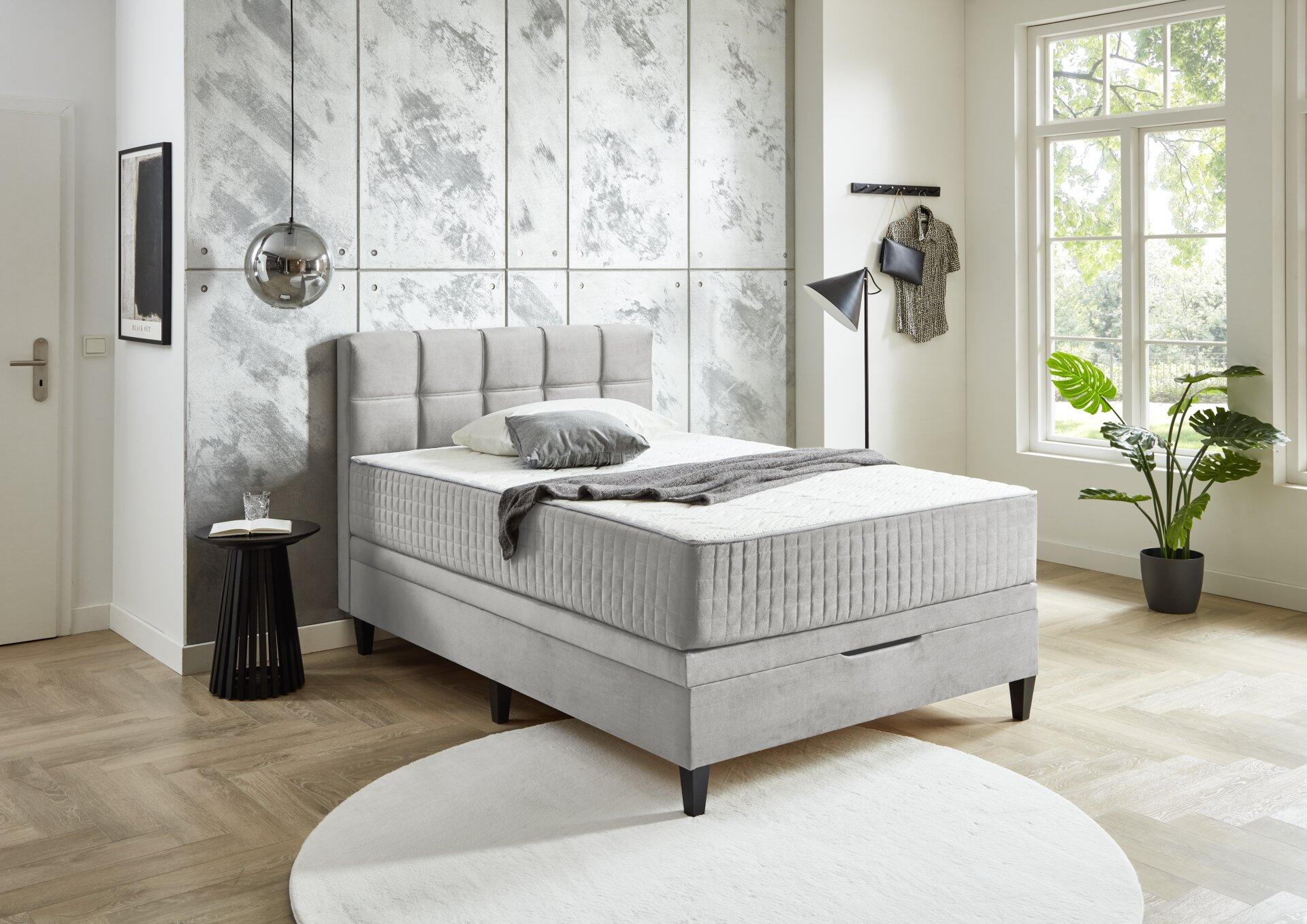 Boxspringbett Wien BX2590 mit grau-anthrazitfarbenem Samtbezug, vertikalem Kopfteil und integriertem Bettkasten, dargestellt aus leicht seitlicher Perspektive in einem modernen Schlafzimmer.