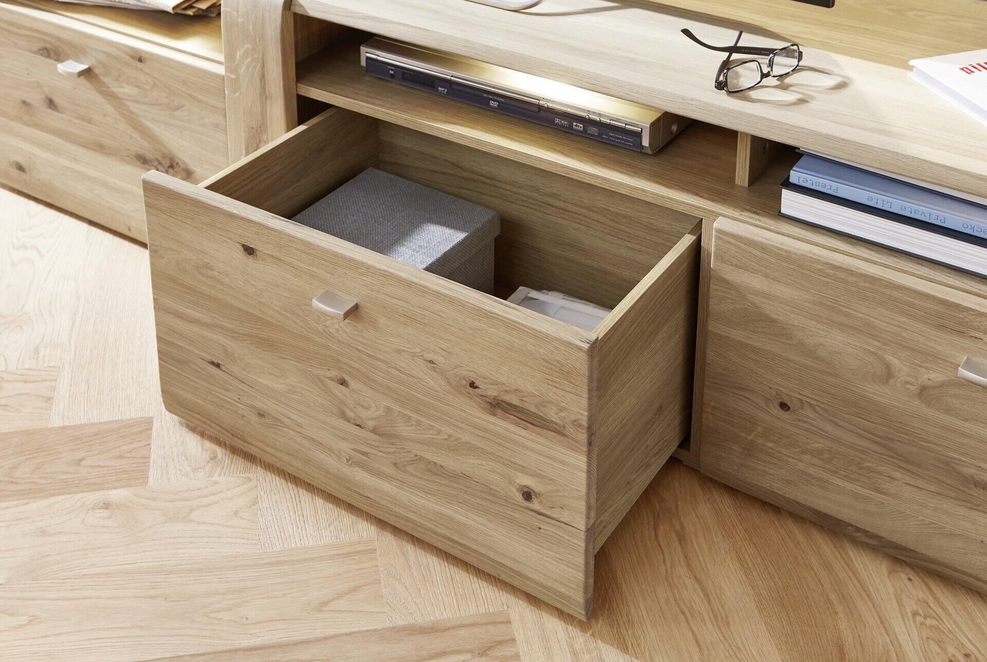 Geöffnete Schublade des TV-Unterschrank Colorado aus massivem, geöltem Altholz mit eingelassenem Holzgriff und grauem Innenleben.
