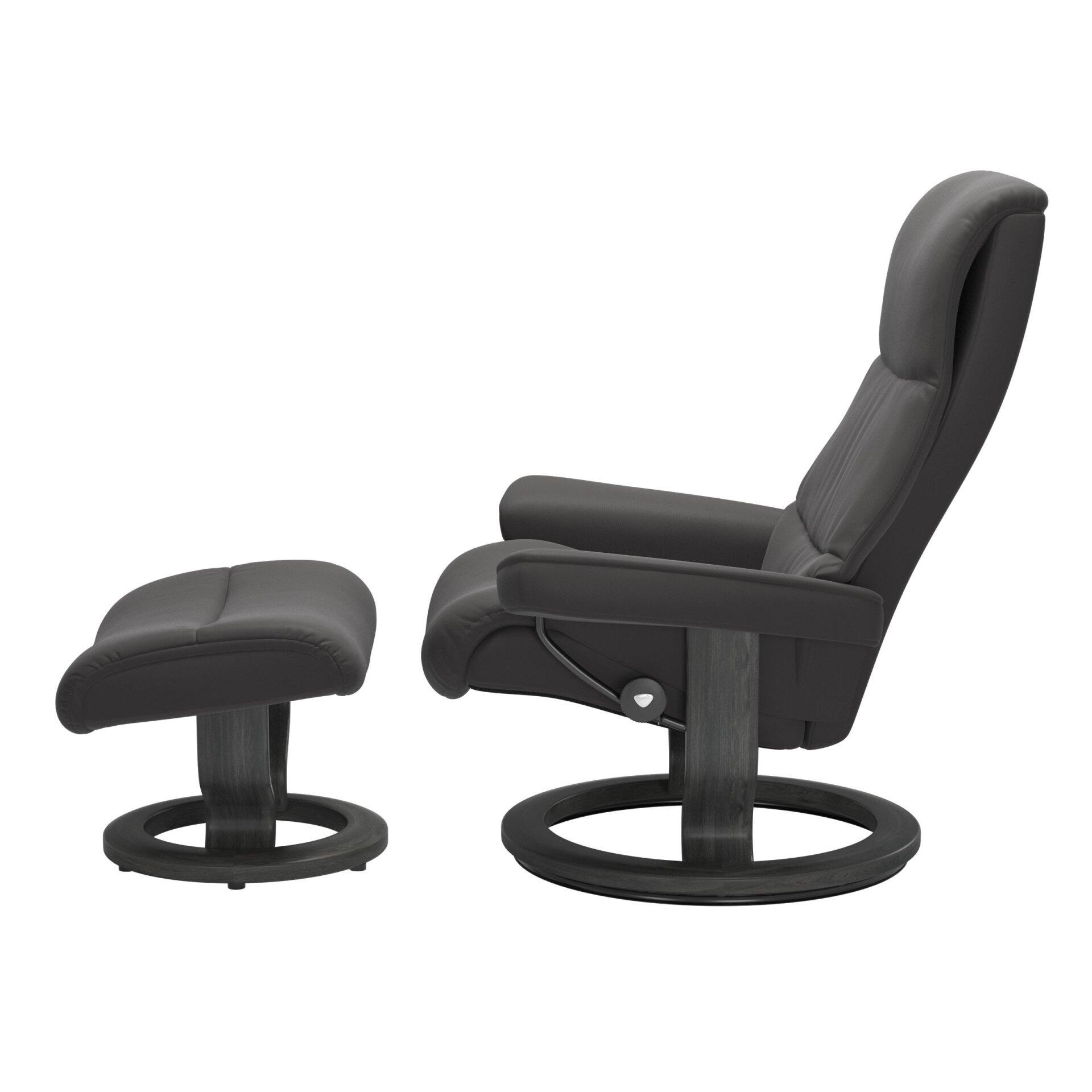 Relaxsessel View mit Fußhocker im Detail: Dunkelgrauer Sessel mit hoher, gebogener Rückenlehne und breiten Armlehnen, sowie Fußhocker mit runder Basis, zeigt die 360° Drehfunktion und Bedienelement für die Relaxfunktion.