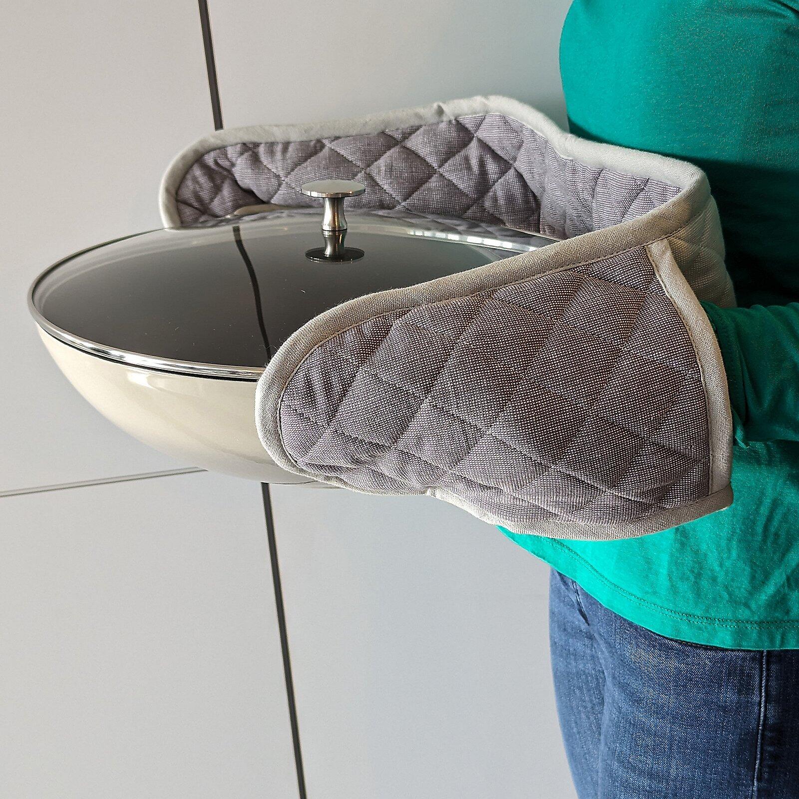 Grauer, gesteppter Ofenhandschuh hält Edelstahl-Kochtopf mit Glasdeckel.