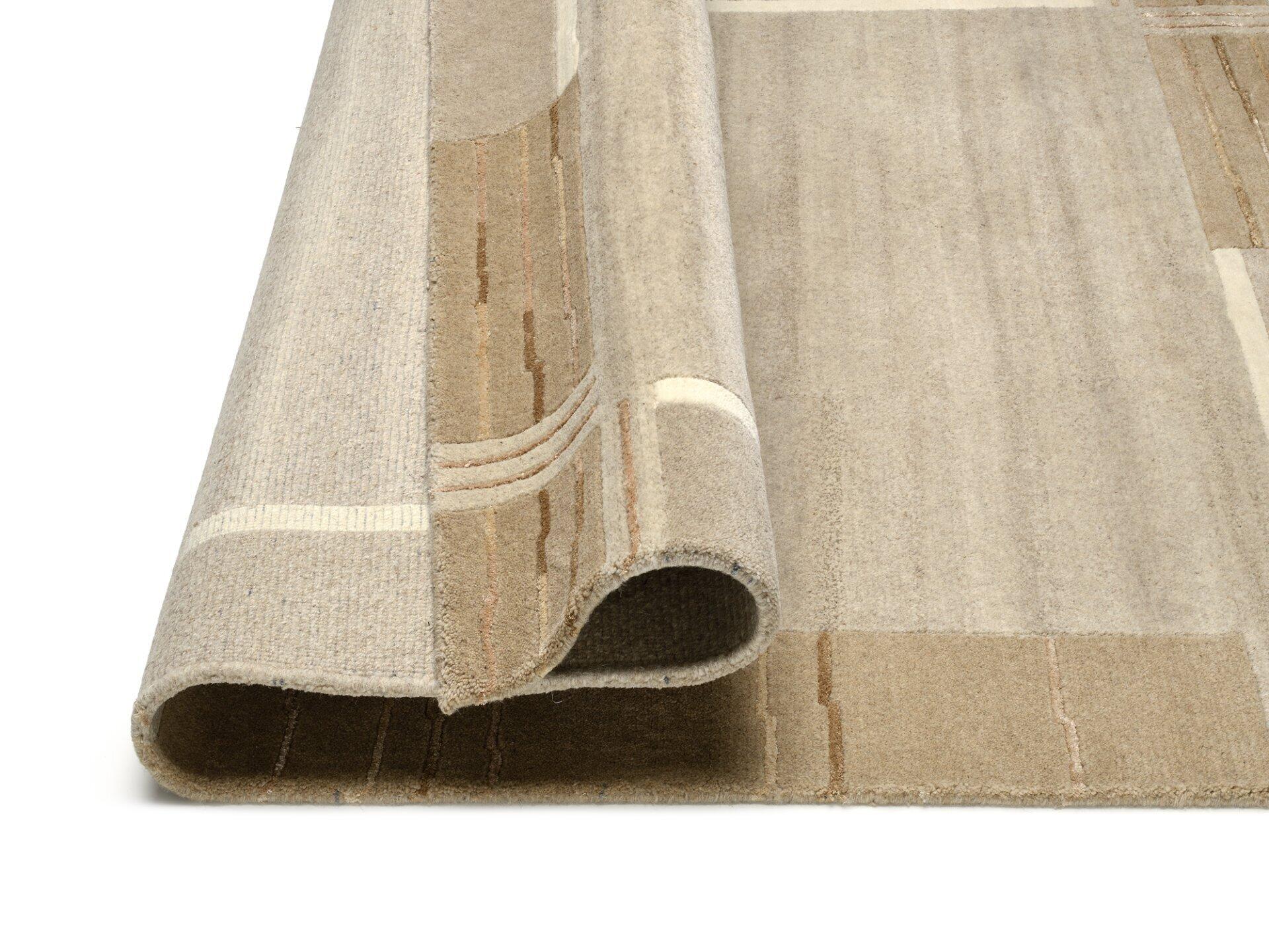 Handgeknüpfter Wollteppich Nanded, aufgerollt, zeigt die Dicke und strukturierte Oberfläche in warmem Beige.