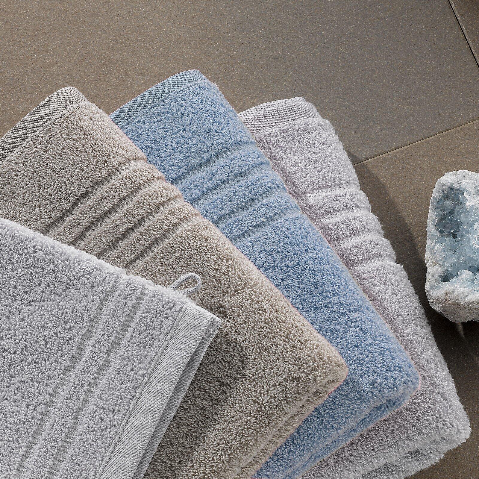 Stapel handgelegter Duschtücher Leonora in hellgrau, beige und hellblau mit feiner Rippstruktur auf grauem Fliesenboden.