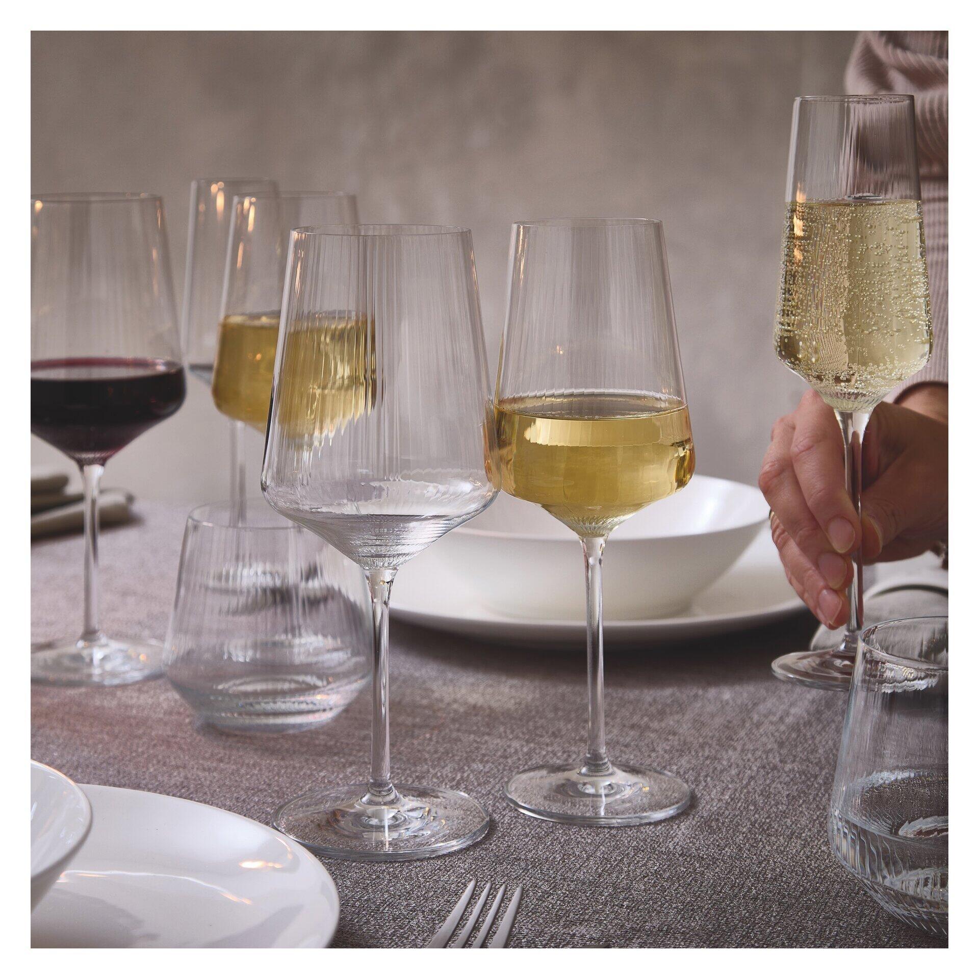 Stilvolle Tischaufstellung mit Champagnergläsern aus transparentem Glas mit geriffelter Textur, präsentiert in einer eleganten Szene mit Weinflaschen und Besteck.