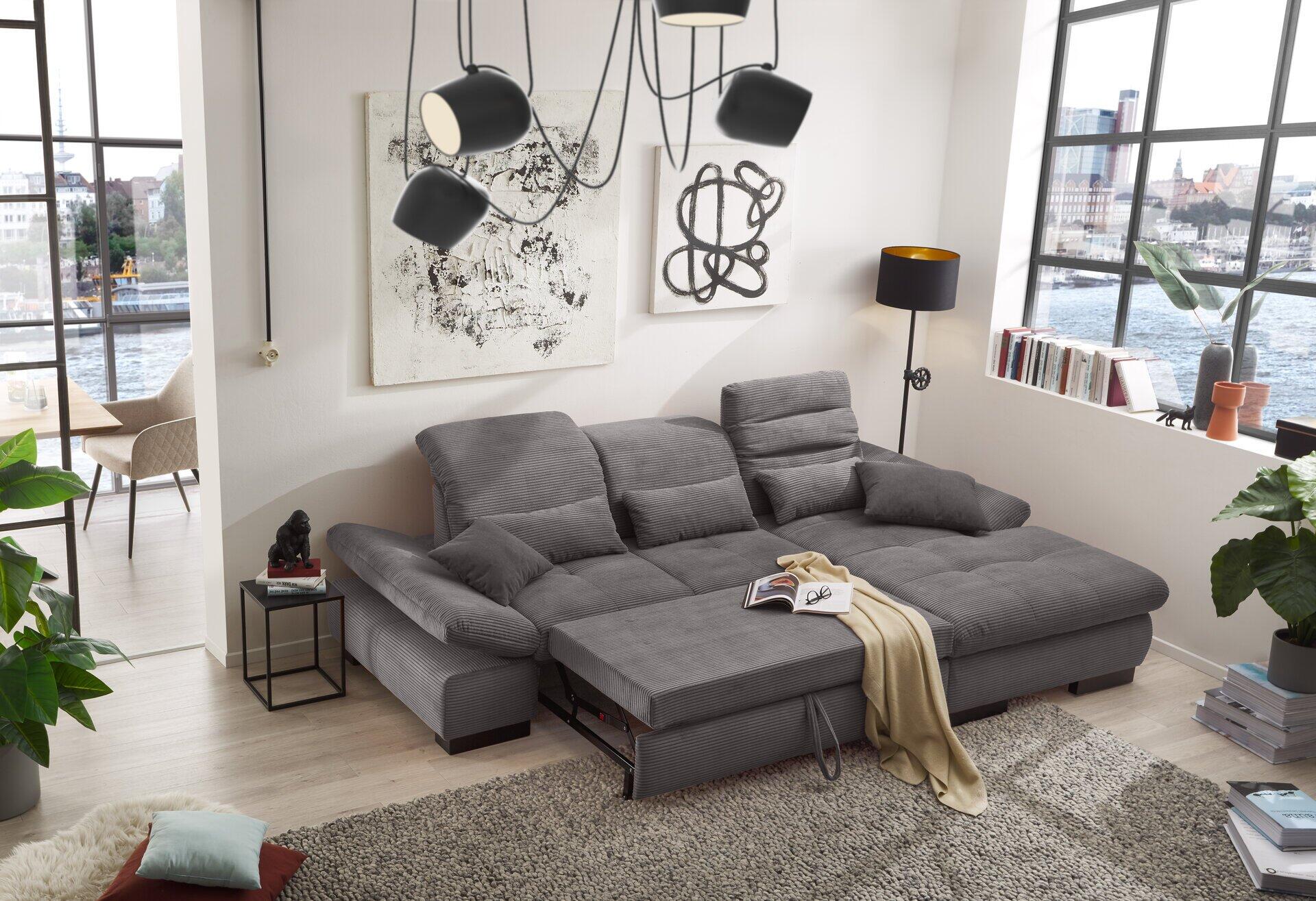 Graue Eckcouch SO 4100 mit segmentierten Sitzflächen und hochklappbarer Schlaffläche, gezeigt aus einer Frontlinksposition im hellen Wohnzimmer.