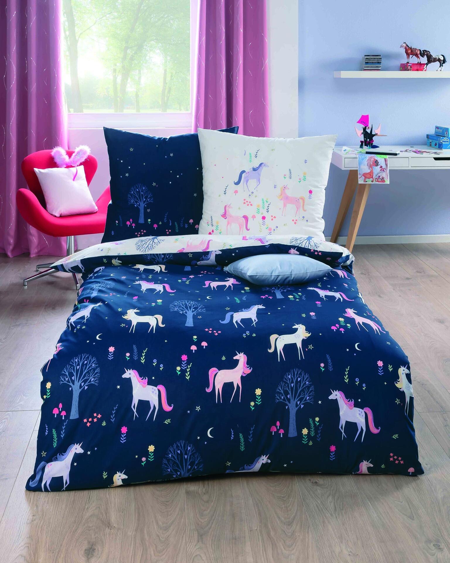 Bettwäsche Zauberwald: Dunkelblaues Bett mit aufgesticktem Einhorn-Motiv aus weißen Einhornhöfen, Sternen, Bäumen und Blüten, detailliert aus erhöhter Perspektive.