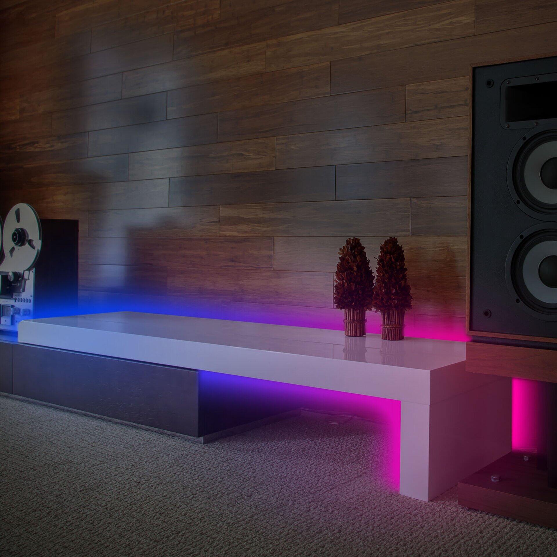 LED Band Magic, weiße TV-Konsole mit integrierter, zweifarbiger LED-Beleuchtung in Blau und Pink, Frontansicht leicht von links versetzt.
