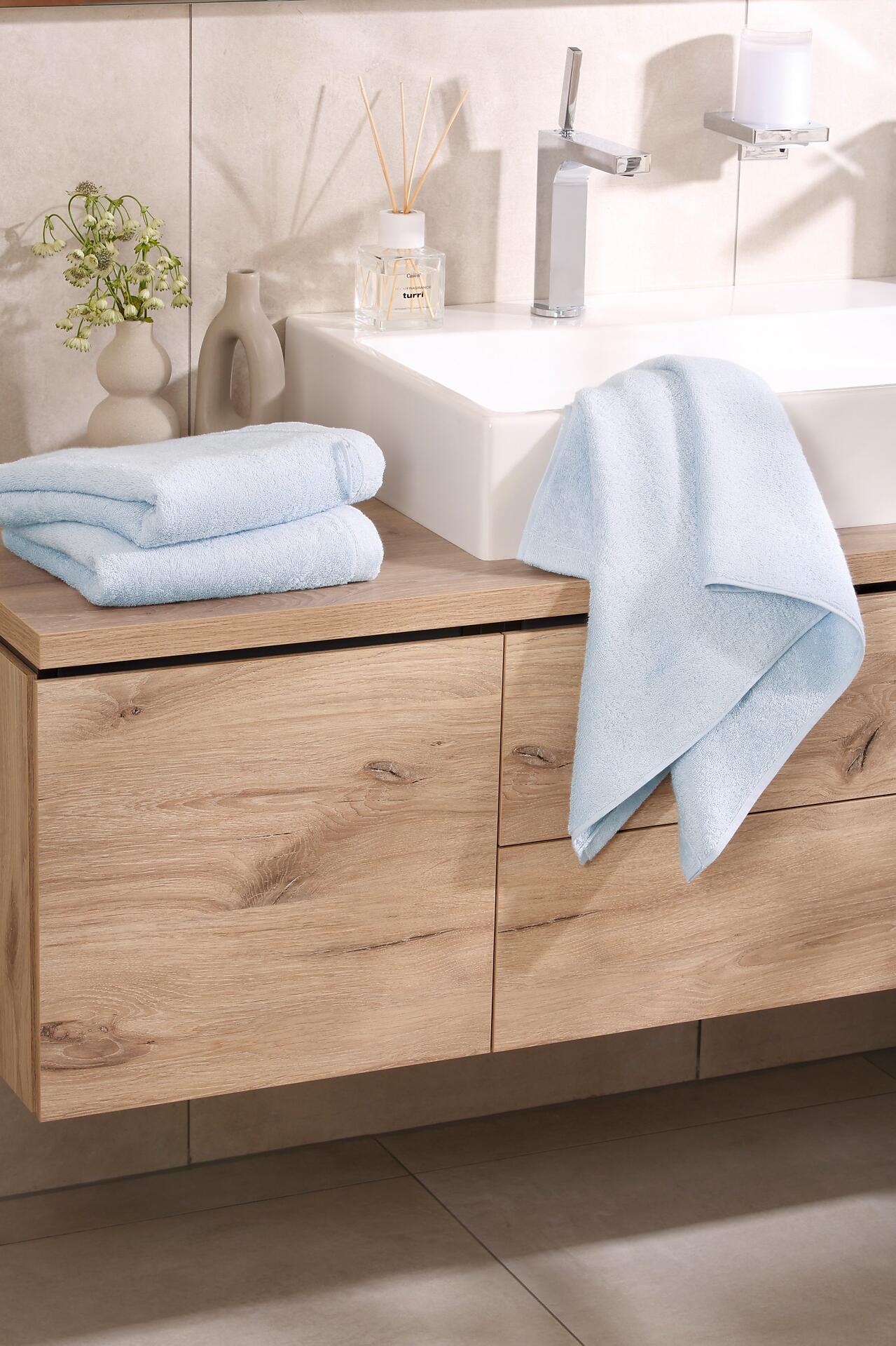 Badezimmerschrank Cawö Gästetuch Lifestyle mit hellen Holzdruck, integrierter Waschtätfläche und Platz für Handtücher.
