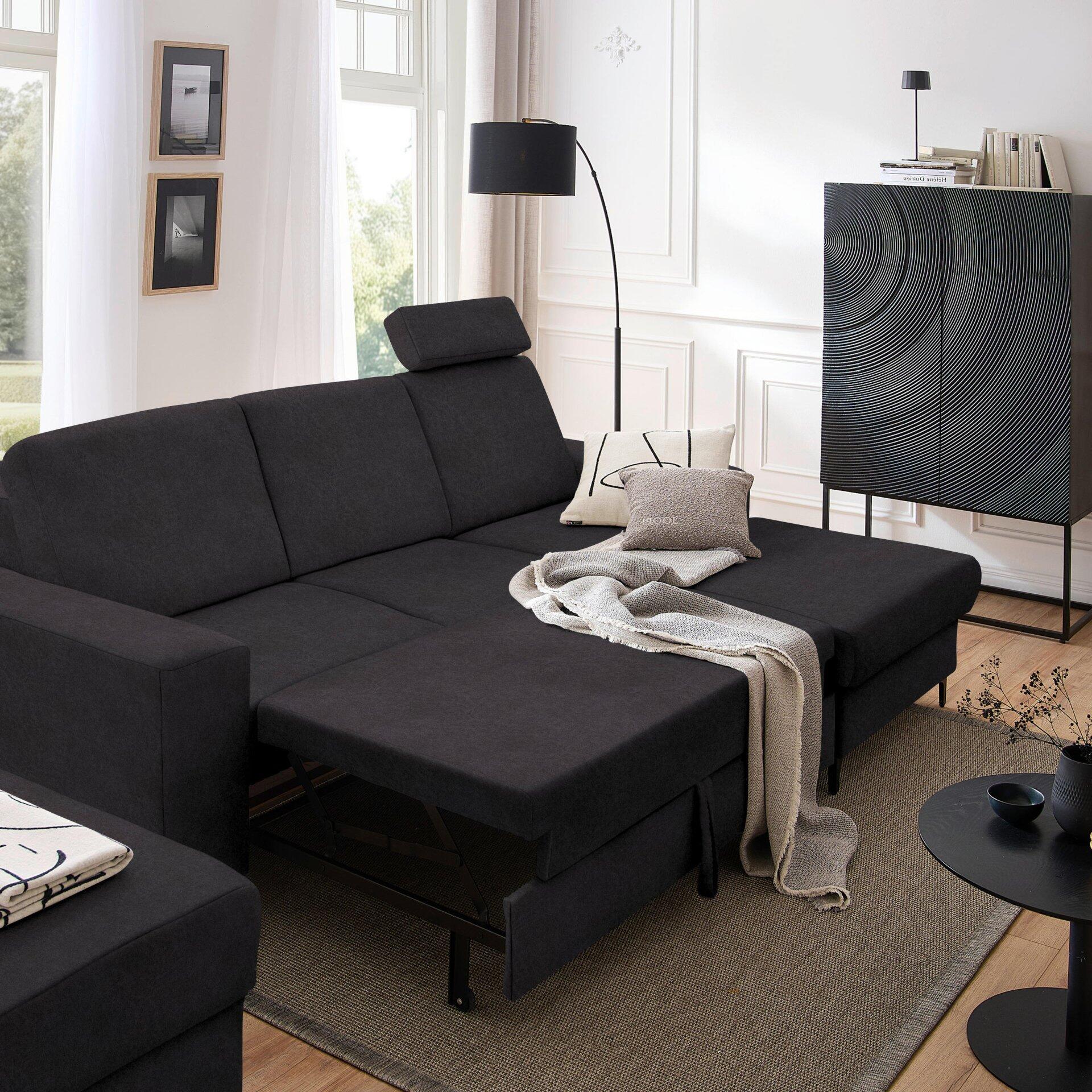 Ecksofa Balina in Grau mit ausgezogener Schlaffläche und Winkelfüßen, präsentiert in einer Innenraumgestaltung mit Teppich und Couchtisch.