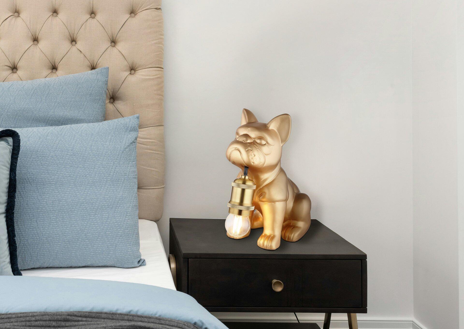 Goldfarbene DOGO Tischleuchte im Bulldoggen-Design auf einem Nachttisch, mit abwärts gerichtetem Lichtschein und E27 Fassung.