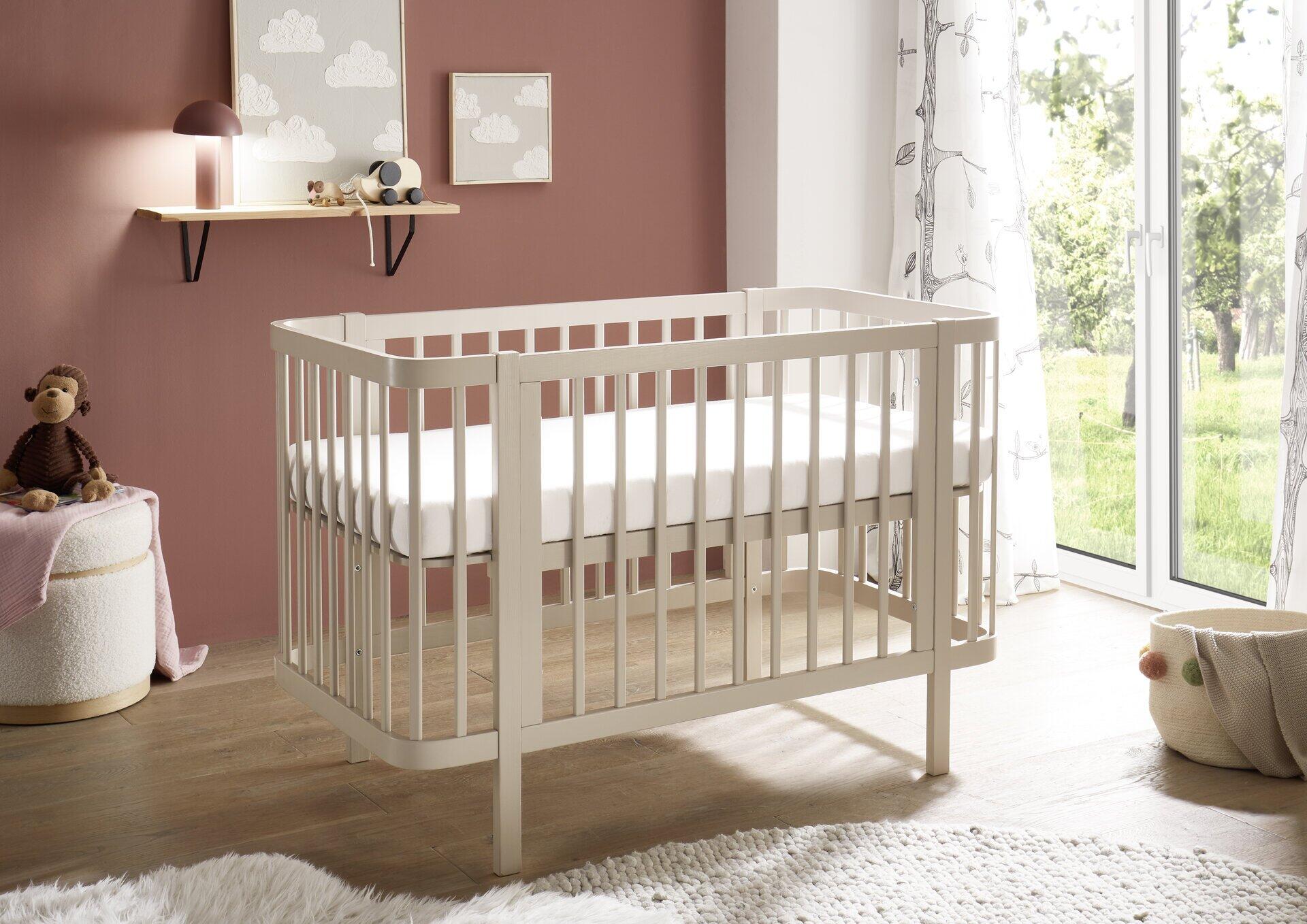 Babybett Peppini mit Umbauseite, aus hellem Holz, seitliche Perspektive im hellen Kinderzimmer.