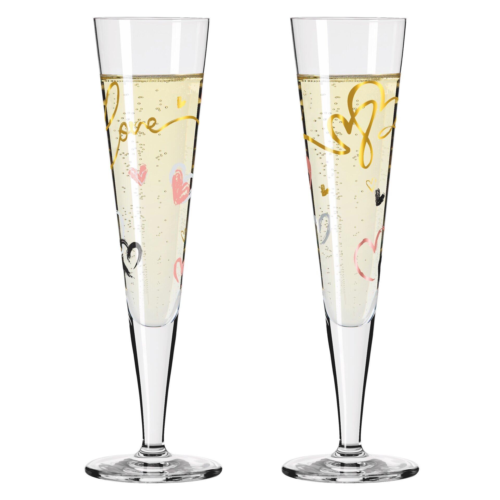 Zwei hoch und schlanke Champagnergläser mit goldenen Schriftzügen und Herzmotiven, gefüllt mit perlendem Getränk, dargestellt aus der Seitenperspektive in einer Geschenkbox.