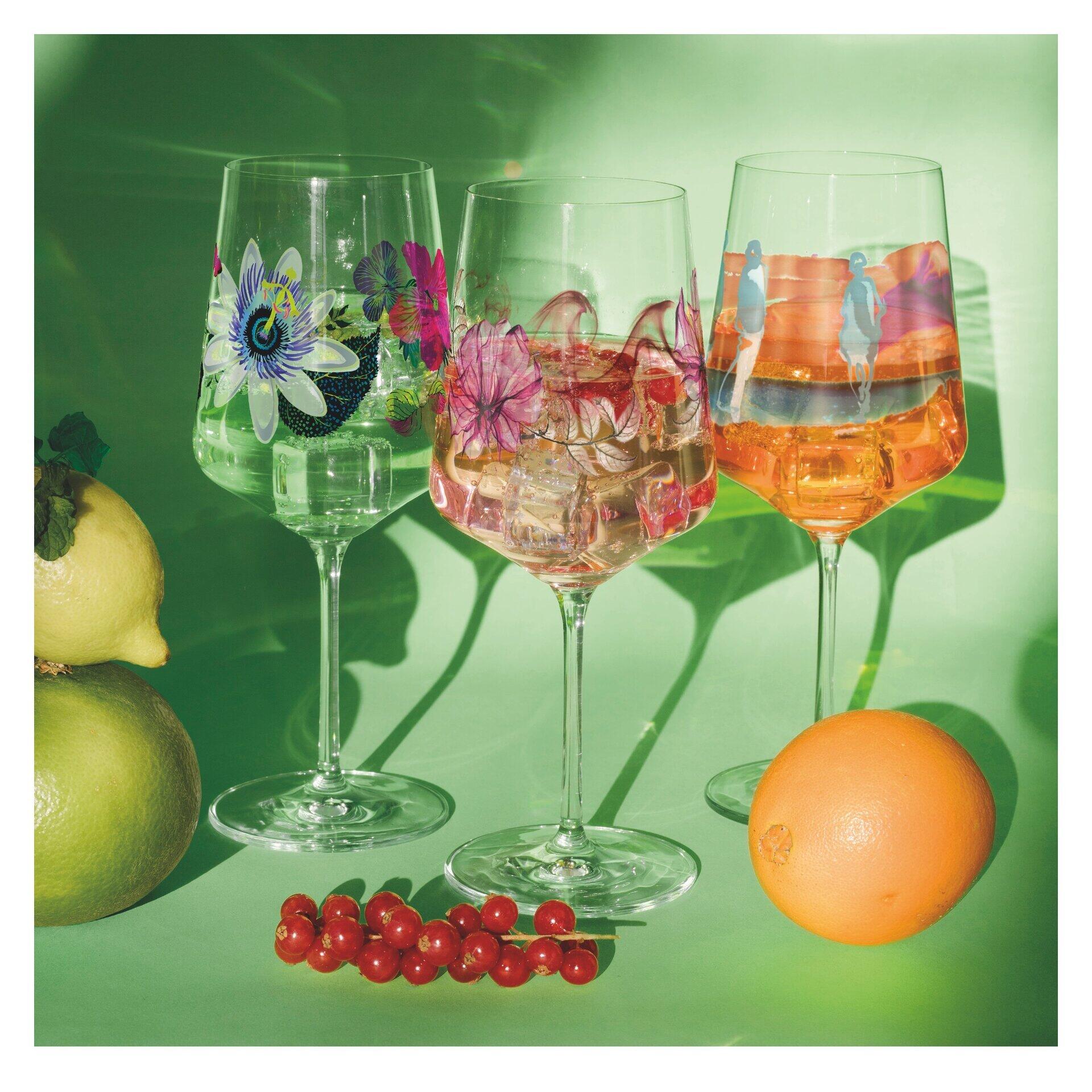 Aperitifglas-Set mit floralen Mustern in Blau, Pink und Orange, dargestellt auf einer leicht erhöhten Perspektive vor einem grünen Hintergrund mit dekorativer Früchte- und Blütenfruchthaltung.