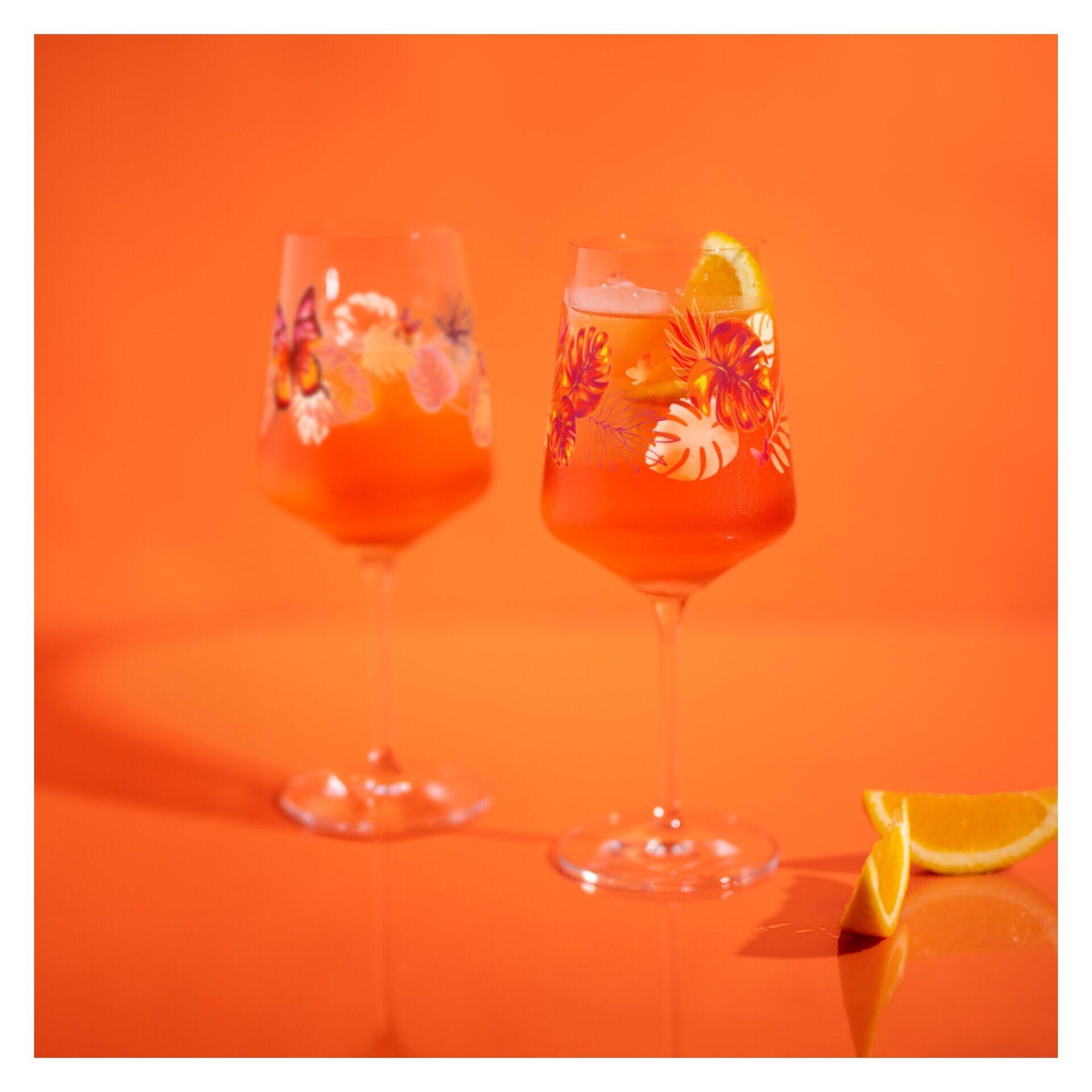 Aperitifglas-Set mit floralem Muster aus Blättern und Blüten, dargestellt auf einer orangefarbenen Oberfläche mit einem Glas gefüllt mit Orangenscheiben.
