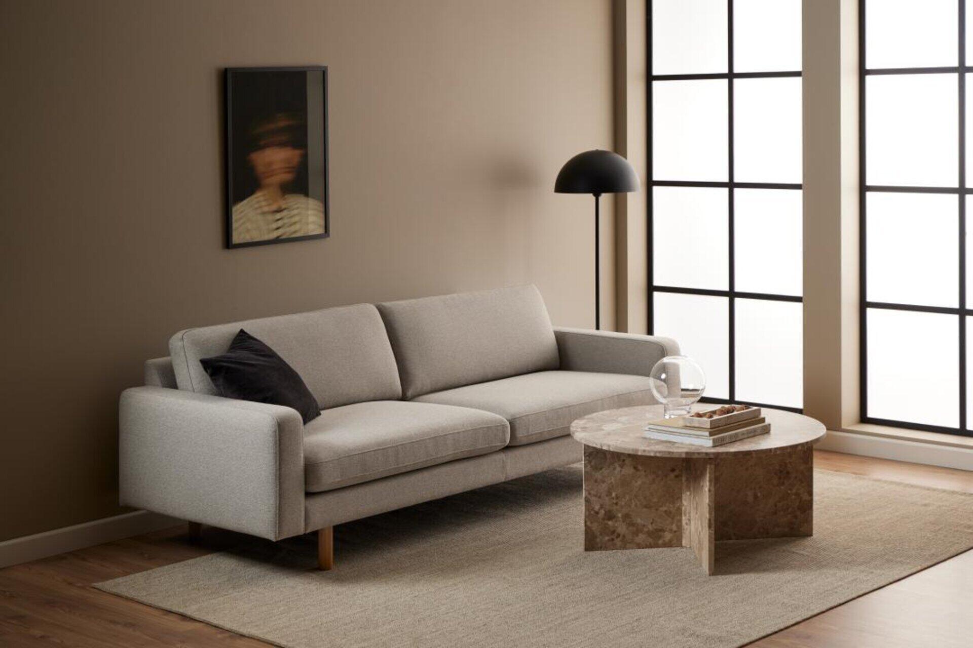 Moderner Couchtisch Vega mit runder Marmorplatte und schwarzer Metallbasis vor einer grauen 3-Sitzer Couch mit hellen Holzfüßen.