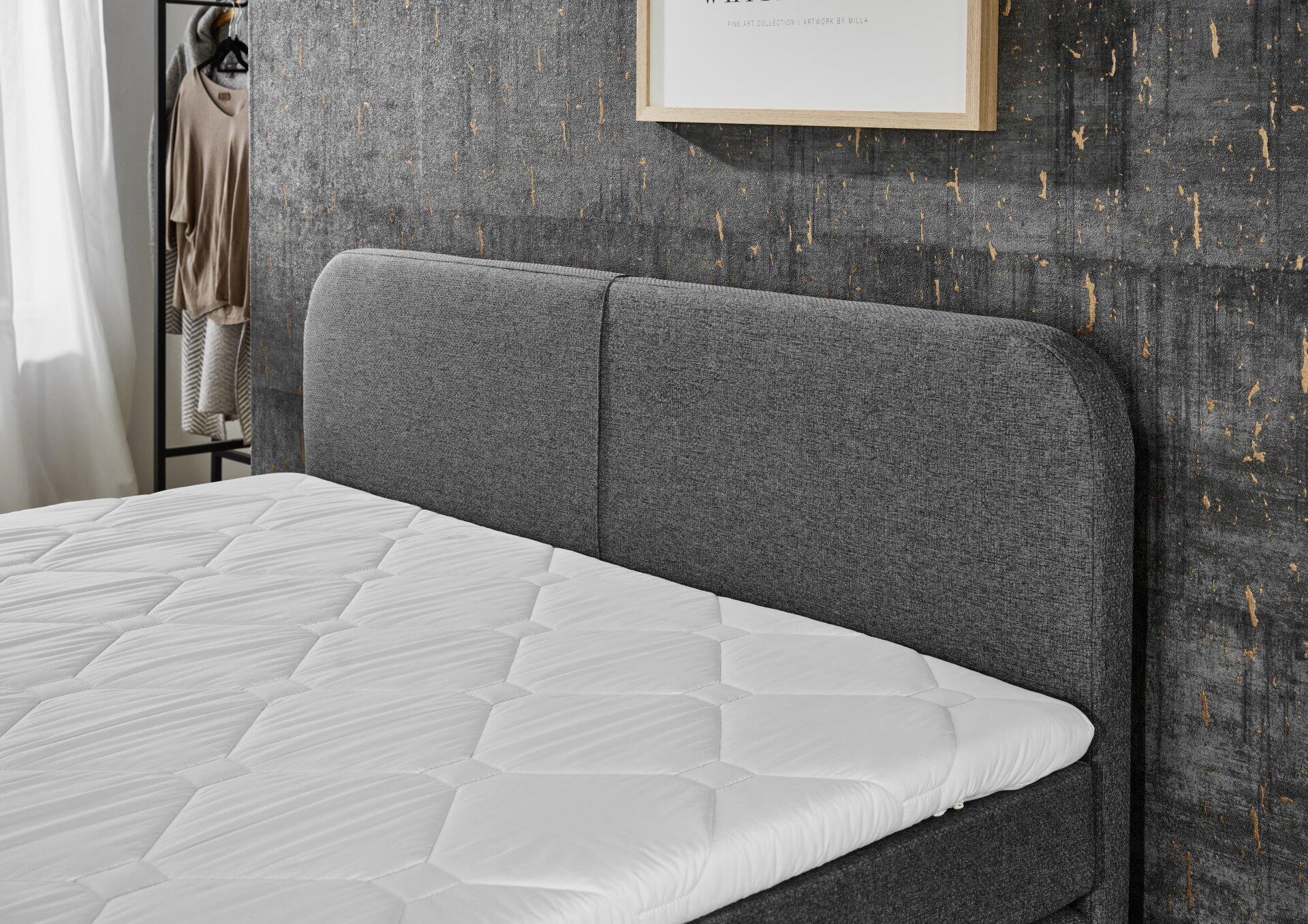 Boxspringbett Joliet BX2410 mit grauem Stoffbezug und diamantförmigem Steppmuster am hoch- und leicht geneigten Kopfteil.