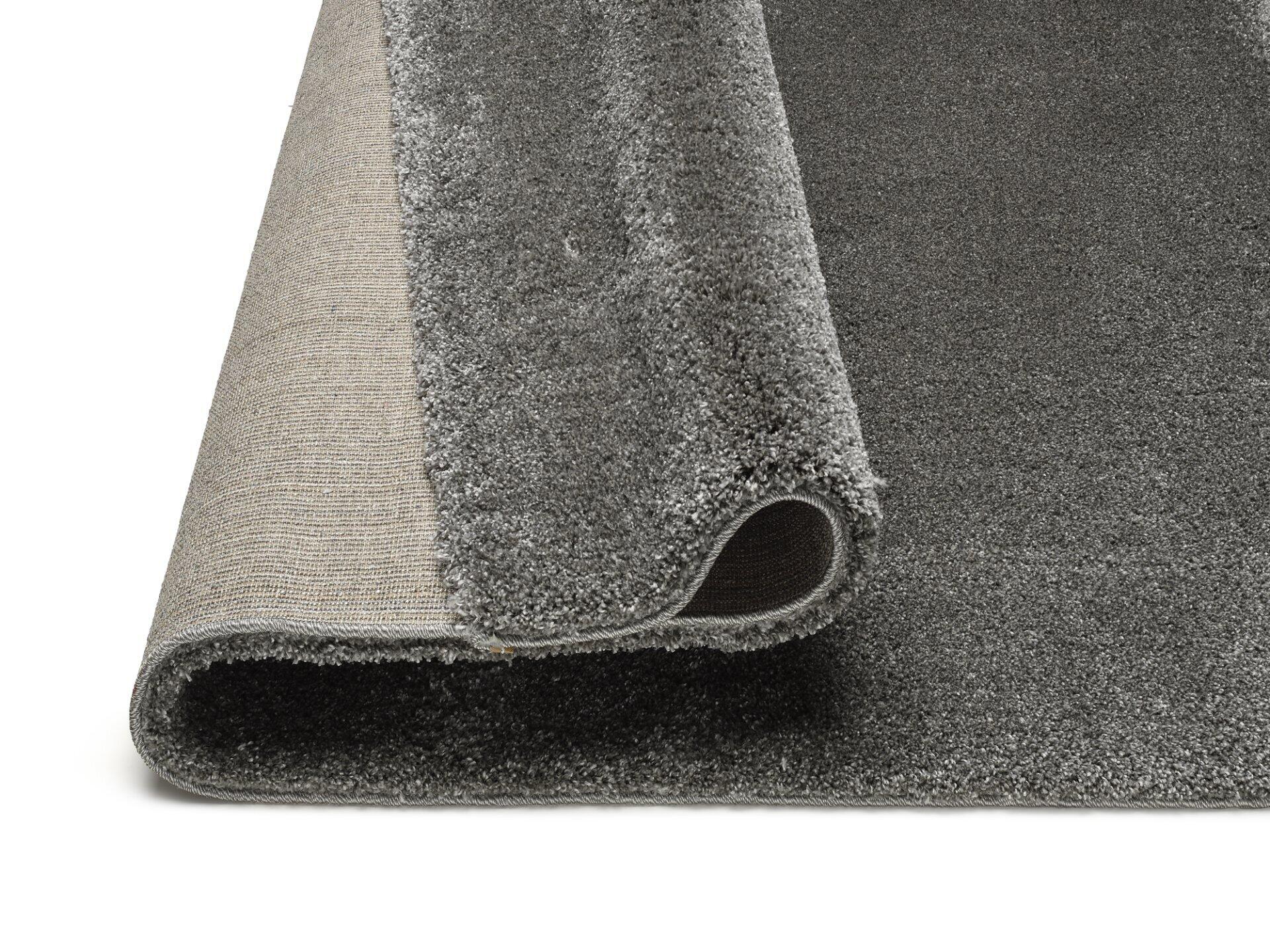 Maschinenwebteppich Erdara: Detailaufnahme des Hochflor-Teppichs mit sichtbarer Ober- und Unterseite, inklusive Details des robusten Gewebes und eines runden Lochs am unteren Rand.