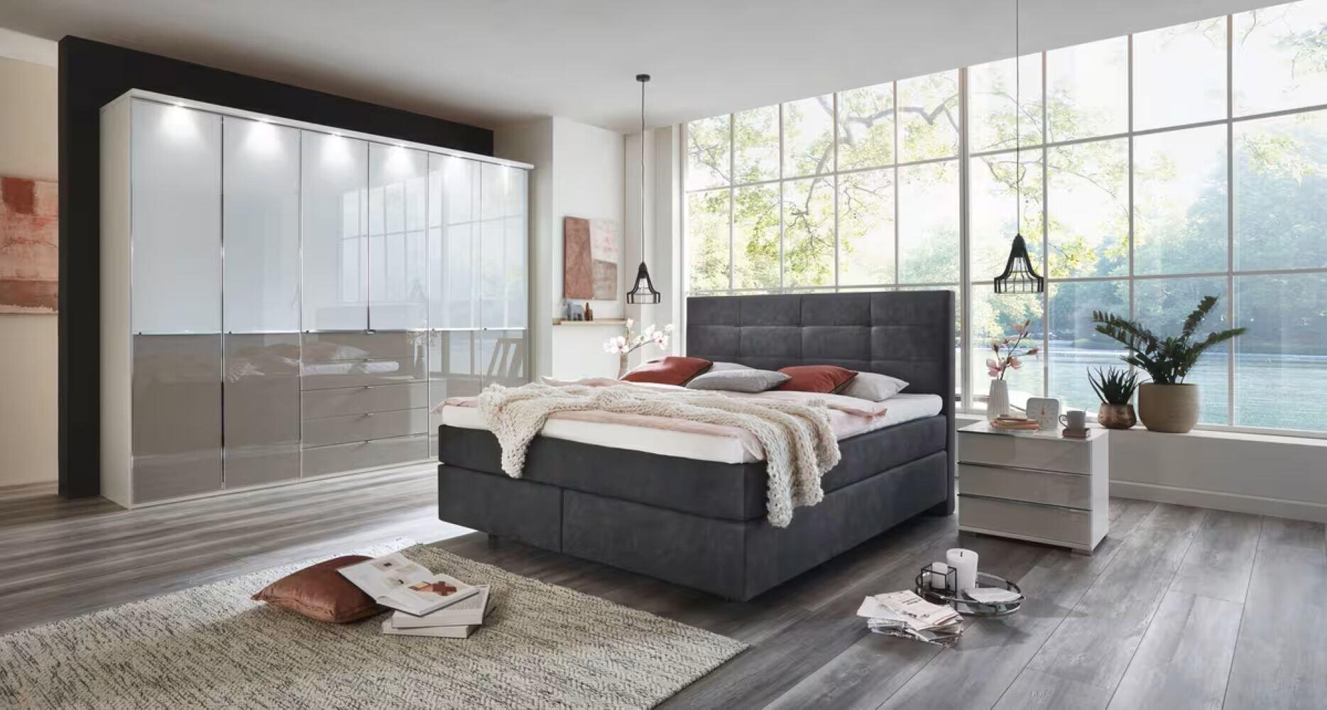 Casa Luna Pro BX5 Boxspringbett mit grauem Foxtrott-Kopfteil und schwebenden Füßen in einem hellen Schlafzimmer mit Kleiderschrank und Nachttisch.