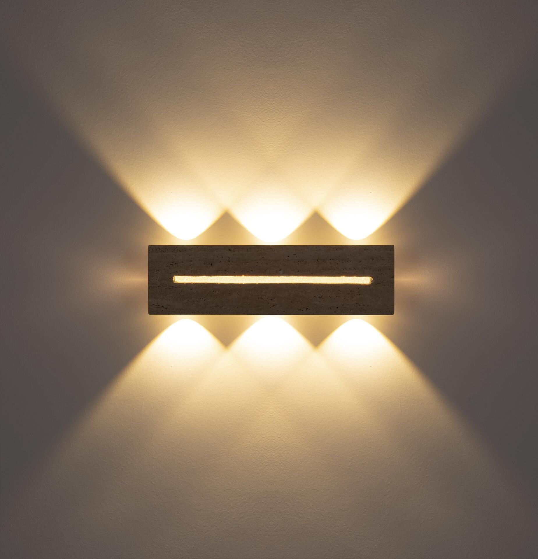 Wandleuchte ROJAS mit Travertin-Glas, die in Frontalperspektive das warme, indirekte Lichtspiel durch drei auf- und abwärts gerichtete Lichtkegel an der Wand zeigt.