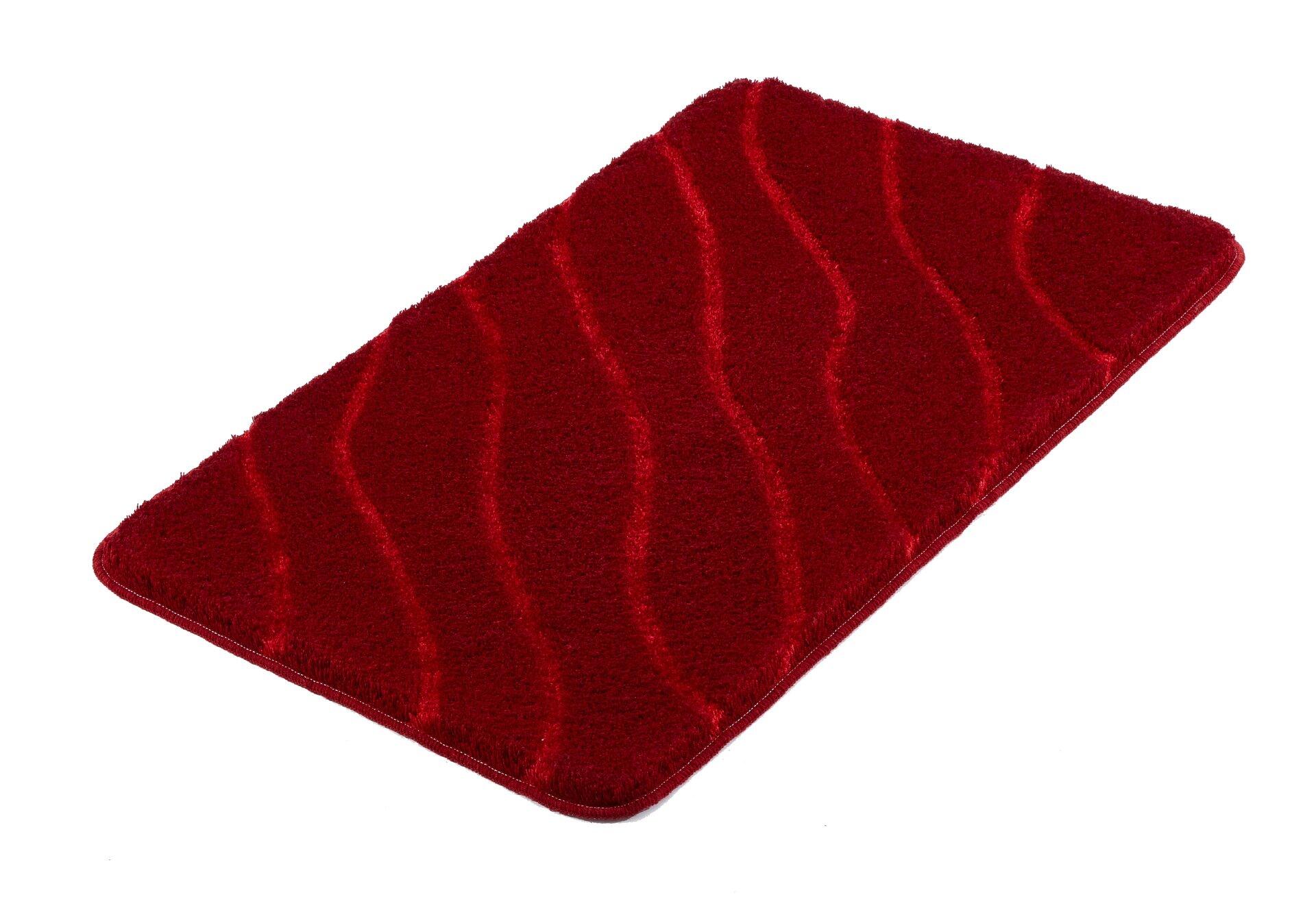 Roter Badteppich "Tram" aus Polyacryl, flauschig und leicht gewellt, in schräger Perspektive auf weißem Hintergrund dargestellt.
