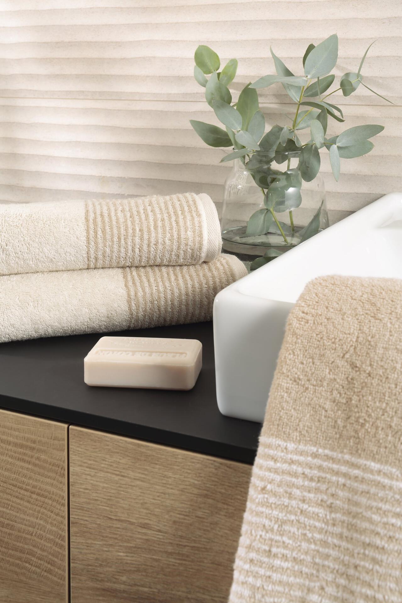 CAWÖ Duschtuch Two-Tone, beige gewickelt auf einem weißen Waschbecken mit strukturierter Oberfläche und Seife.