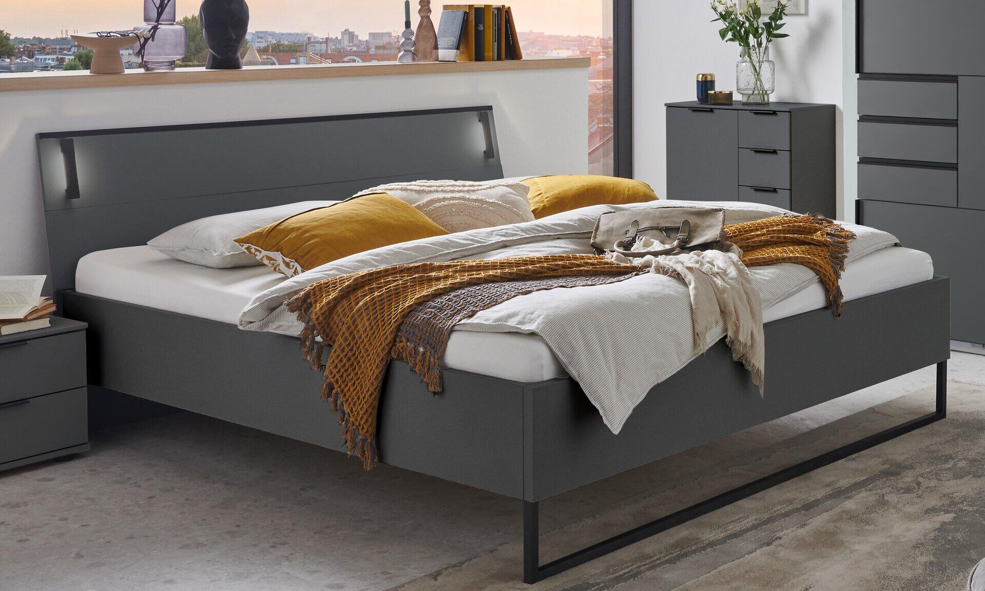 Futonbett Tilburg in Abs. Graphit mit grau lackiertem Rahmen, Kopfteil mit Nische und Nachttisch, Blick auf eine Stadtlandschaft im Hintergrund.