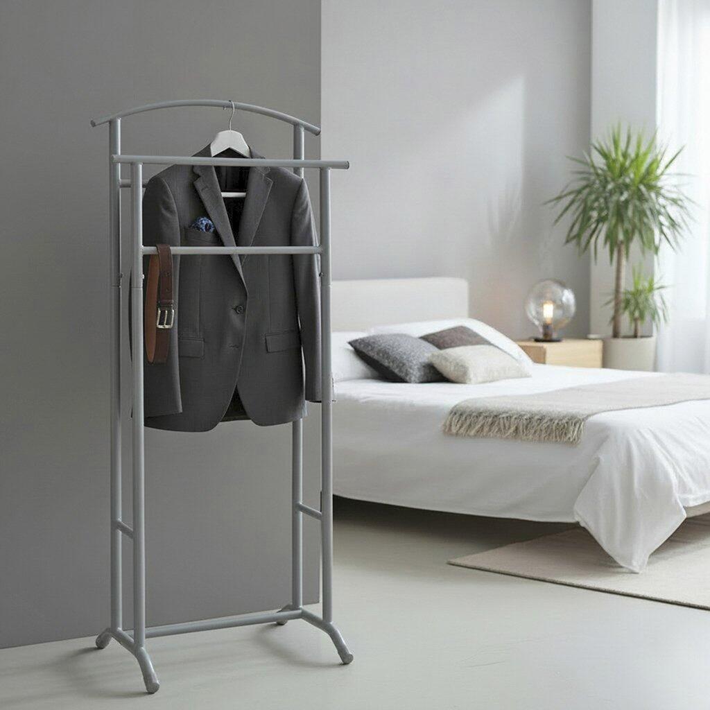 Herrendiener 55103 mit silberfarbenem Stahlrohrrahmen, zwei Ablageflächen und Kleiderstange, präsentiert auf dem Bild vor einem Bett.