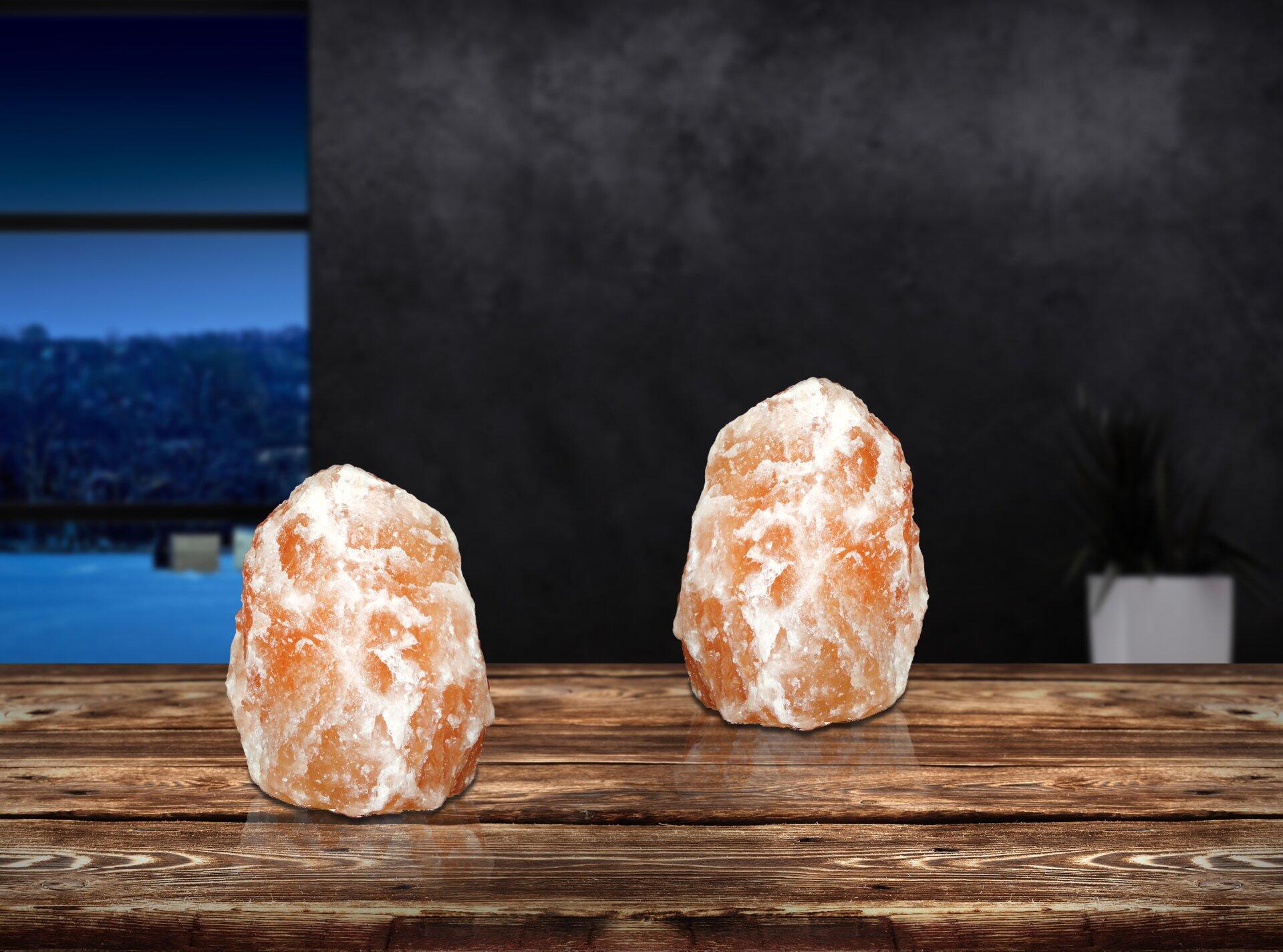 Salzlampen mit warmer Beleuchtung auf einem Holztisch, die die einzigartige, kristalline Oberfläche und die entspannende Atmosphäre der Tischleuchte STONE hervorheben.