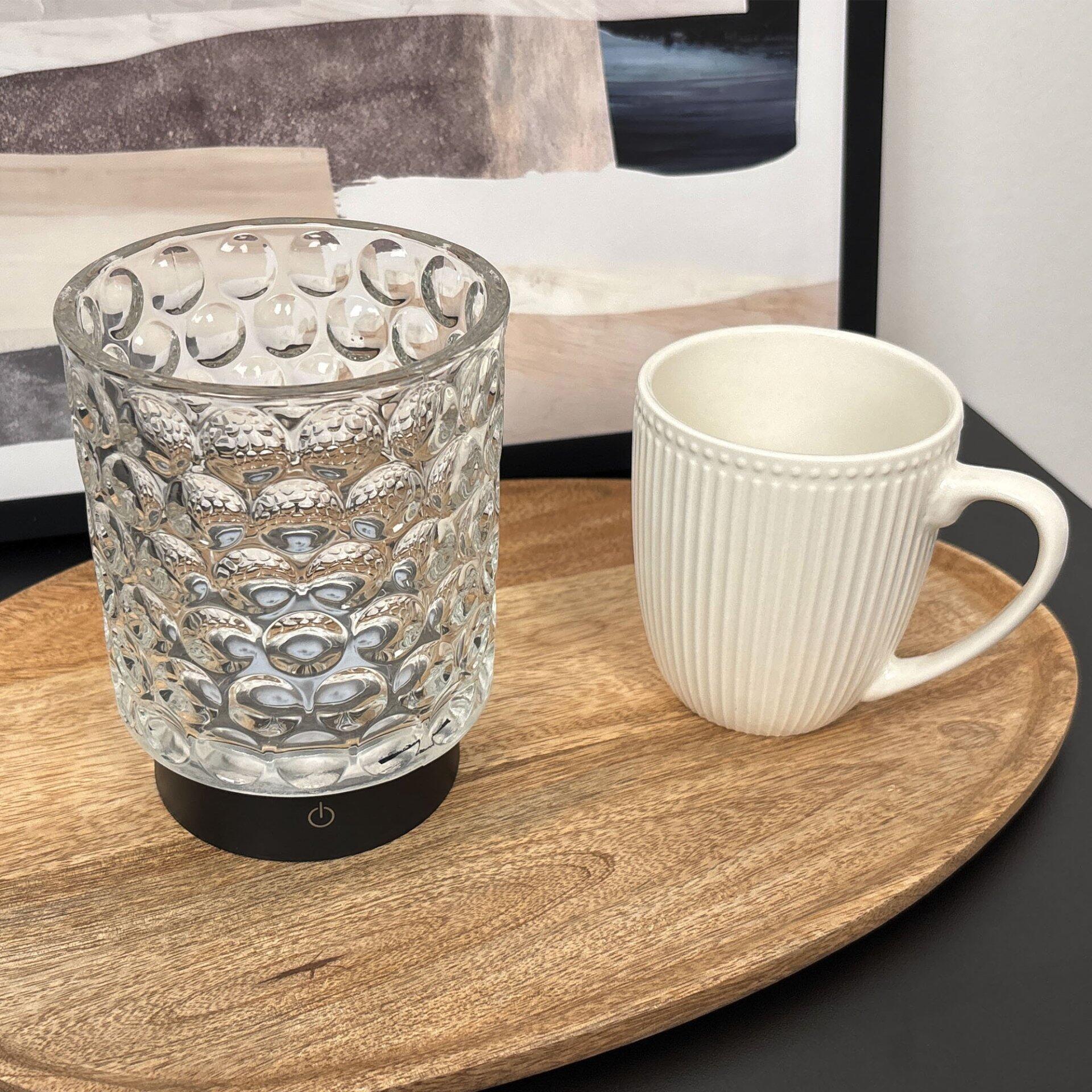 Tischleuchte Sunora mit Glasfuß und Touchdimmer-Knopf auf einem Holztisch, neben einer Keramiktasse.