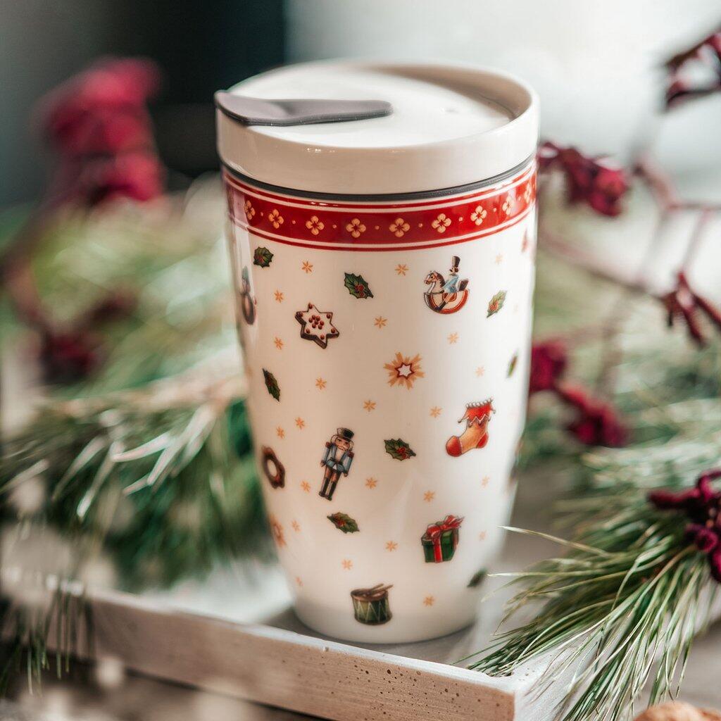 Weihnachtlich dekorierter Becher "Toys Delight" von Villeroy & Boch mit Detailansicht von weihnachtlichen Motiven wie Nussknacker, Weihnachtsmann und Sternen, inklusive Deckel mit Trinkhalm-Schlitz.