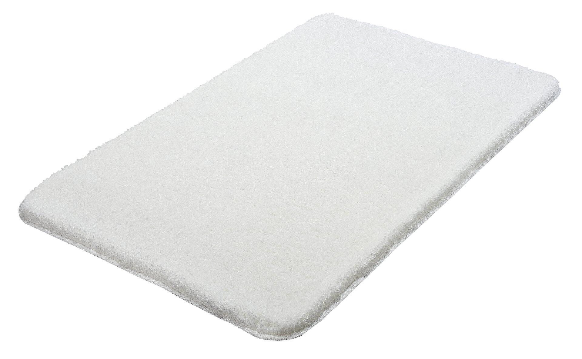 Flauschiger, weißer Badteppich Relax aus Polyacryl mit abgerundeten Kanten und dichter Textur, aus leicht erhöhter, seitlicher Perspektive.