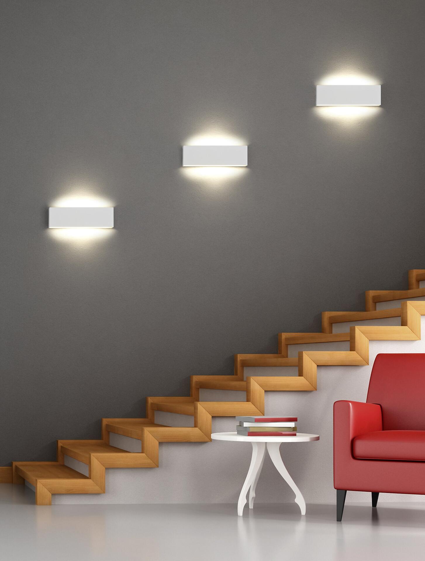 Moderne Wandleuchte Concha mit warmweißem Licht, integriert in eine minimalistische Wandbeleuchtung mit skulpturaler Treppe und roten Akzentmöbeln.
