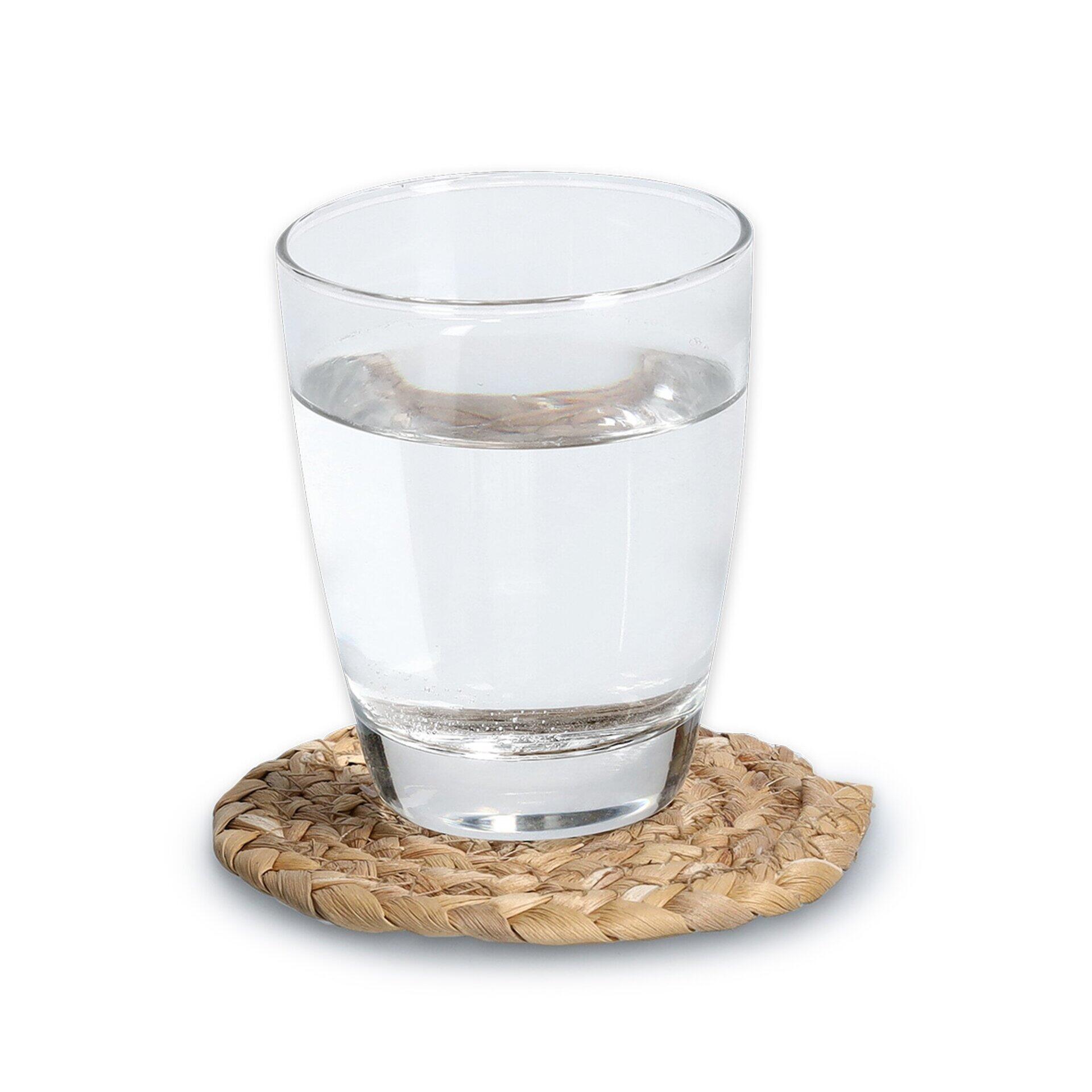Untersetzer aus geflochtenem Naturmaterial schützt den Tisch vor Feuchtigkeit, mit einem darauf stehenden Glas aus einer leicht erhöhten Perspektive.