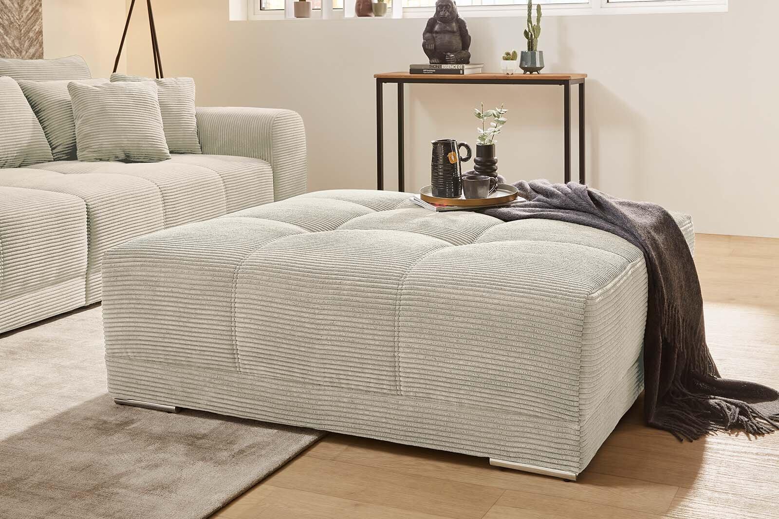 Hocker Moldau mit hellgrauem Cordbezug, chromfarbenen Füßen und abgesteppter Federkernpolsterung, detaillierte Aufnahme mit angrenzendem Sofa und Teppich.