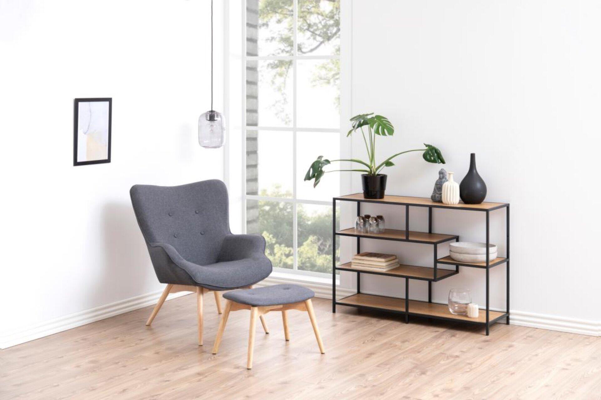 Regal Seaford mit asymmetrischem Design und dekorativen Elementen vor einem grauen Sessel, leicht erhöhte Perspektive.
