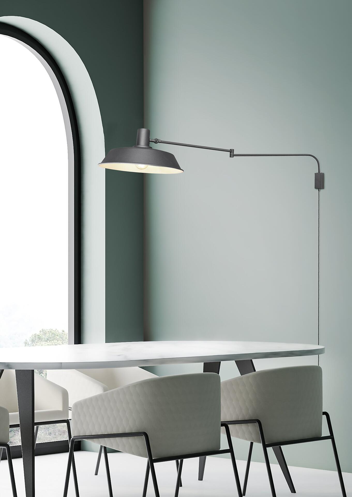 Schwarze Wandleuchte Bolder an der Wand über einem Tisch mit marmorierter Oberfläche und grauen Stühlen, die einen gerichteten Lichtschein abgibt.