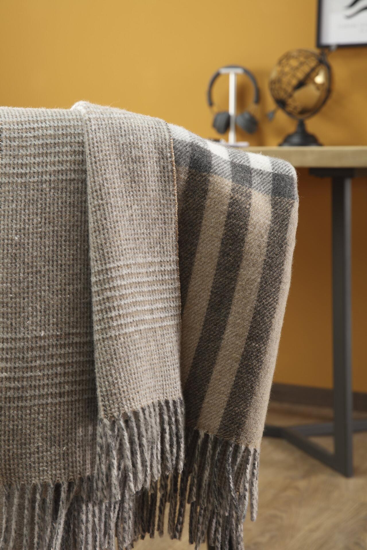 Detailaufnahme des hellbraun und dunkelbraun gestreiften Biederlack Plaids "Twin Check" mit Fransenrand, aus 80% Wolle und 20% Kaschmir, aufgenommen aus einer unteren Perspektive, um die Strickmusterstruktur hervorzuheben.
