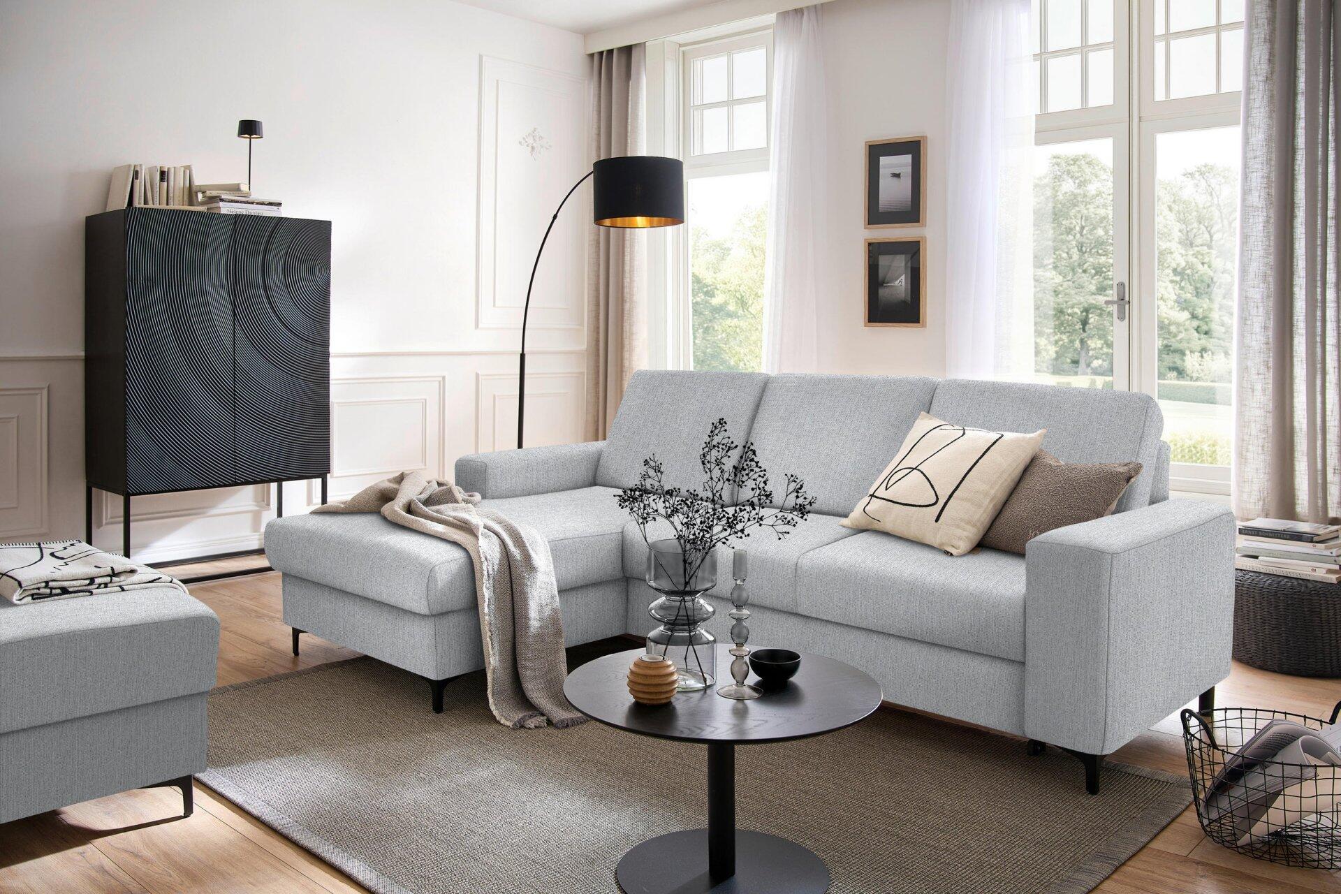 Ecksofa Balina mit niedriger Sitzhöhe, abgerundeten Armlehnen und Bettkasten, im Raumarragement mit Teppich und Beistelltisch.