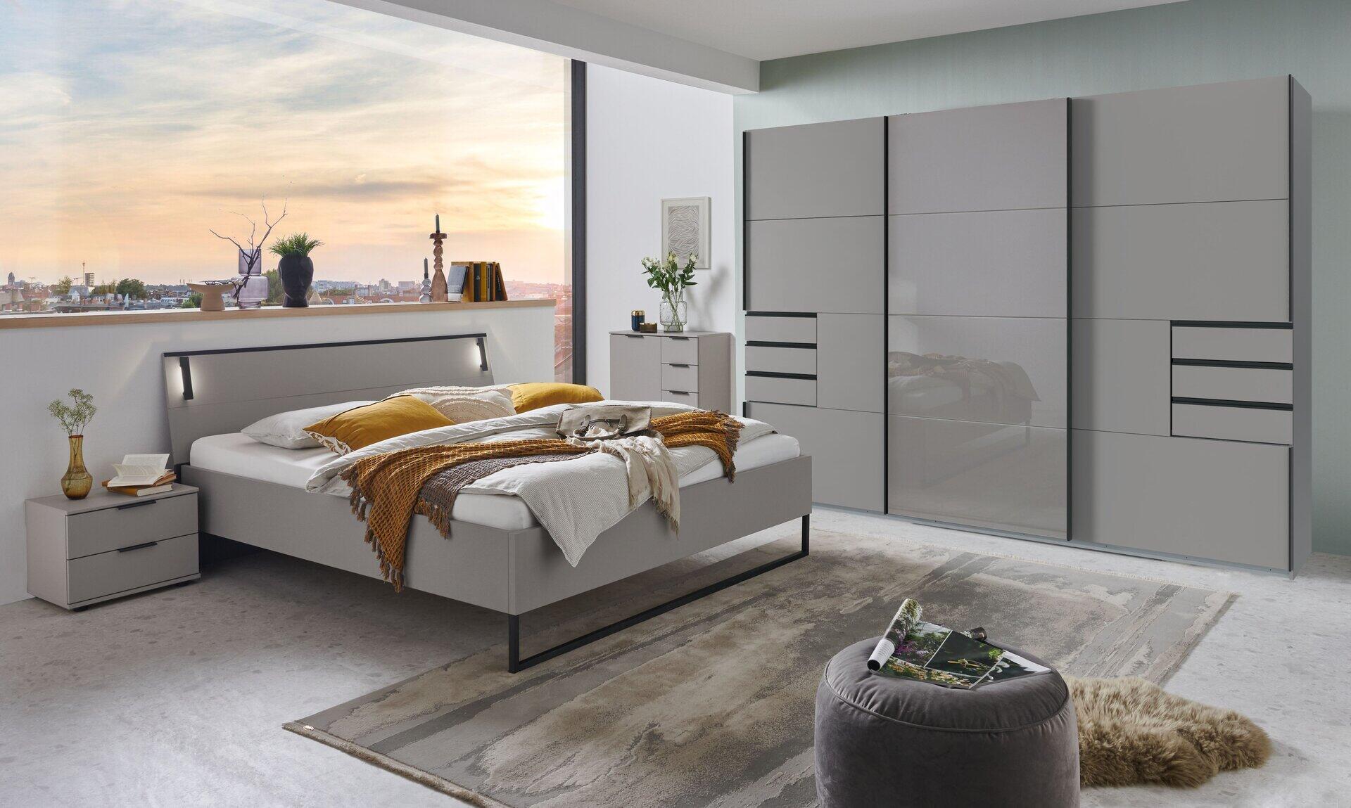 Kleiderschrank Tilburg mit Saharagrauen Glastürfronten und schwarzen Griffen, dargestellt aus erhöhter Perspektive in einem stilvollen Schlafzimmer.