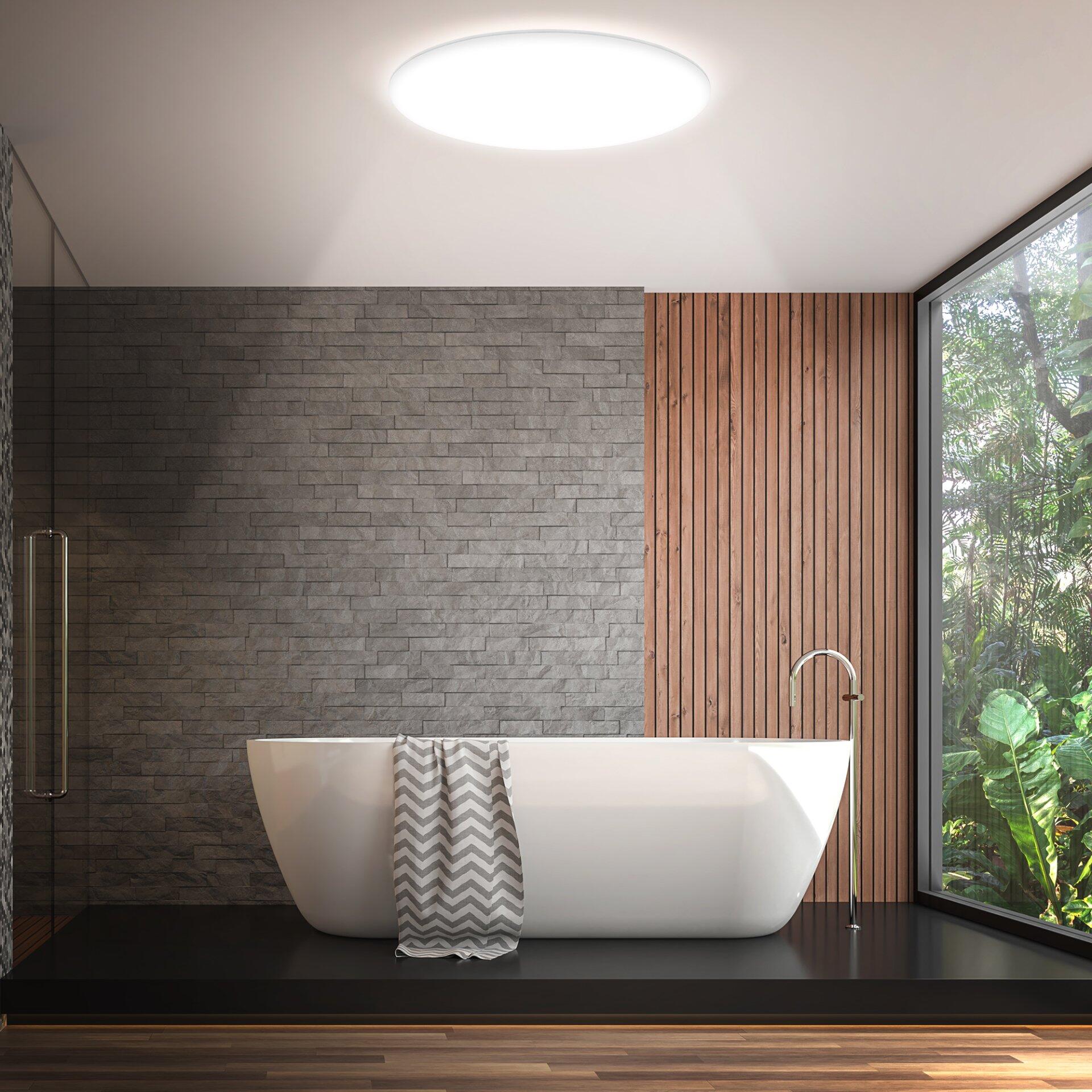 Luxuriöses Badezimmer mit freistehender Keramikbadewanne, Duschkabine und Armatur, beleuchtet von Tageslicht durch ein Fenster mit Blick auf Grünflächen.