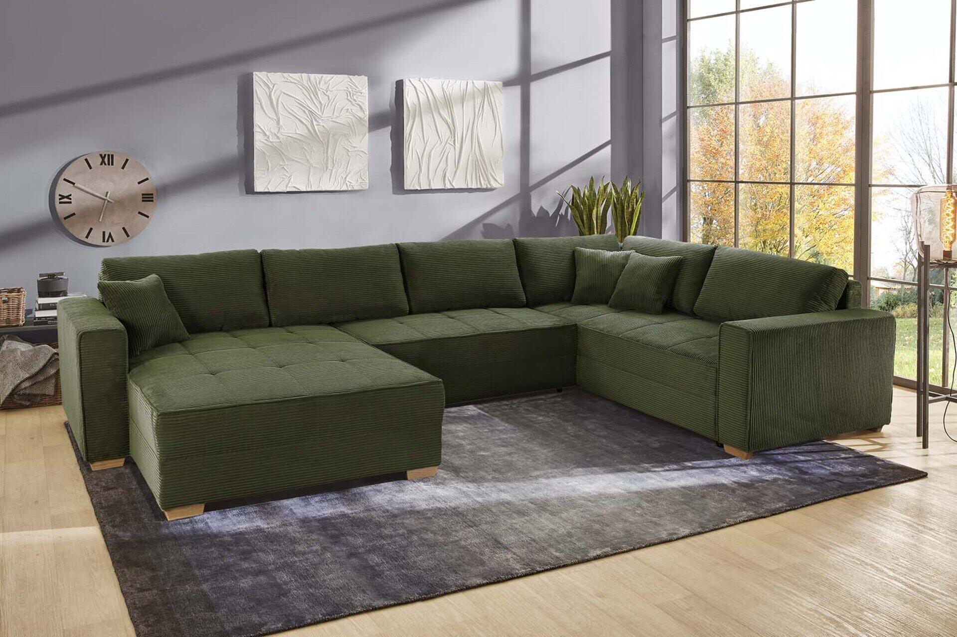 Grüne Wohnlandschaft Brixen mit Cordbezug, Eichenholzfüßen und Chaiselongue, dargestellt aus leicht erhöhter Frontalperspektive in einem modernen Wohnzimmer.